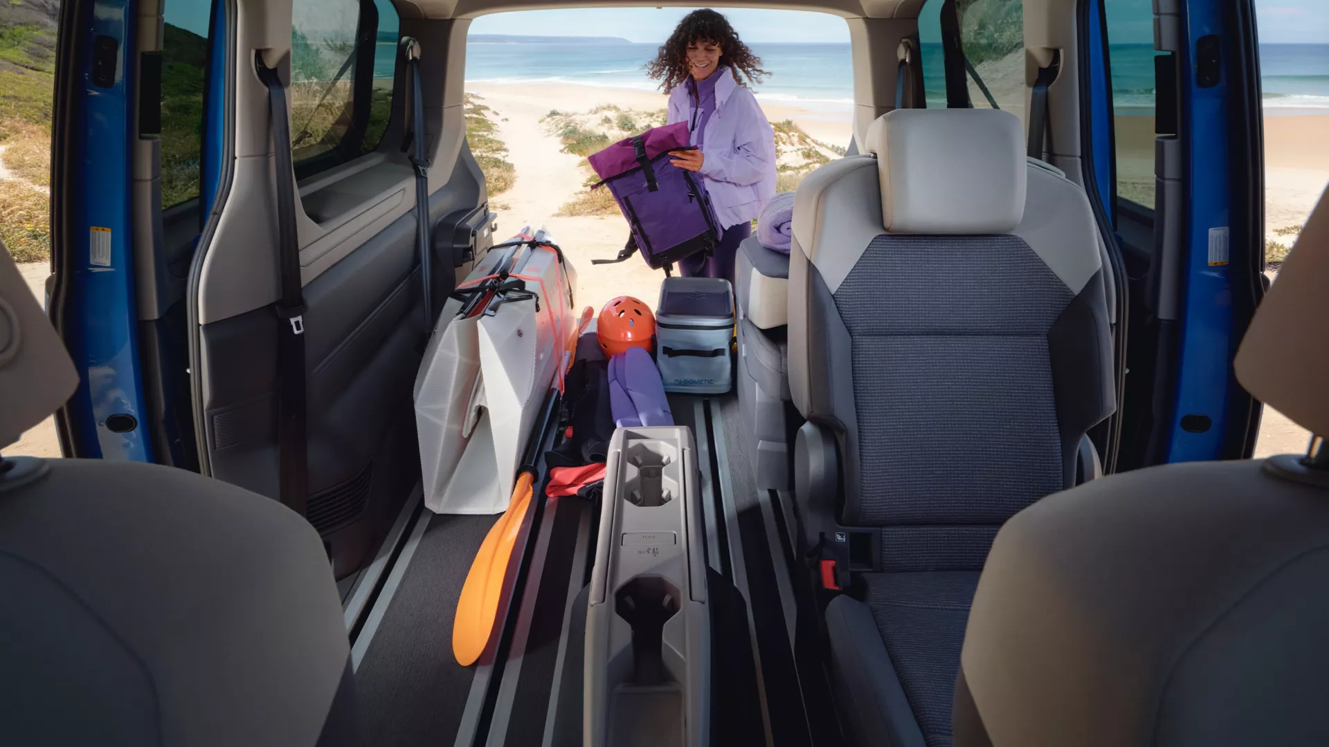 Vista interna di un furgone con una persona in spiaggia.