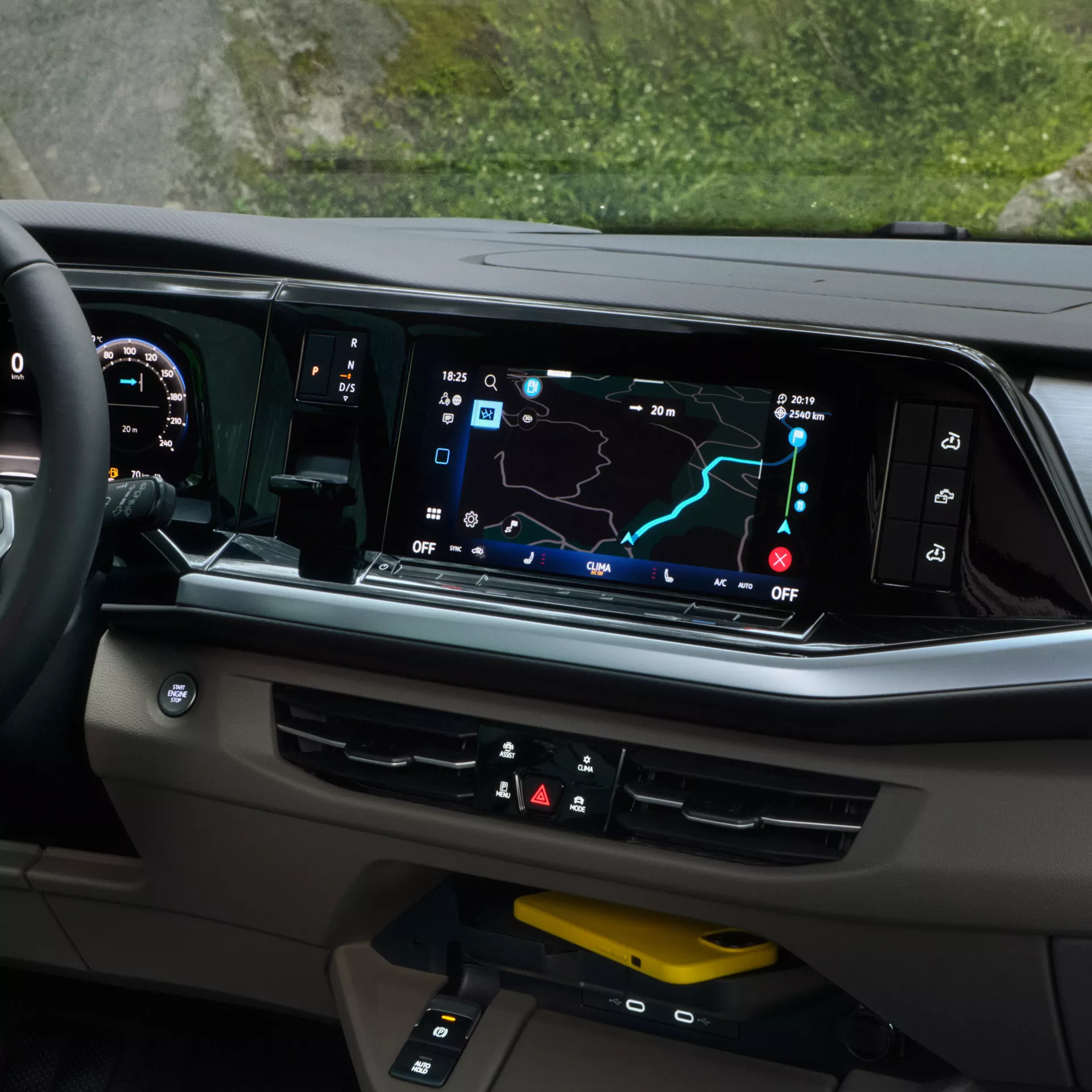 Interni moderni di un veicolo con sistema di navigazione, comandi clima e telefono giallo.