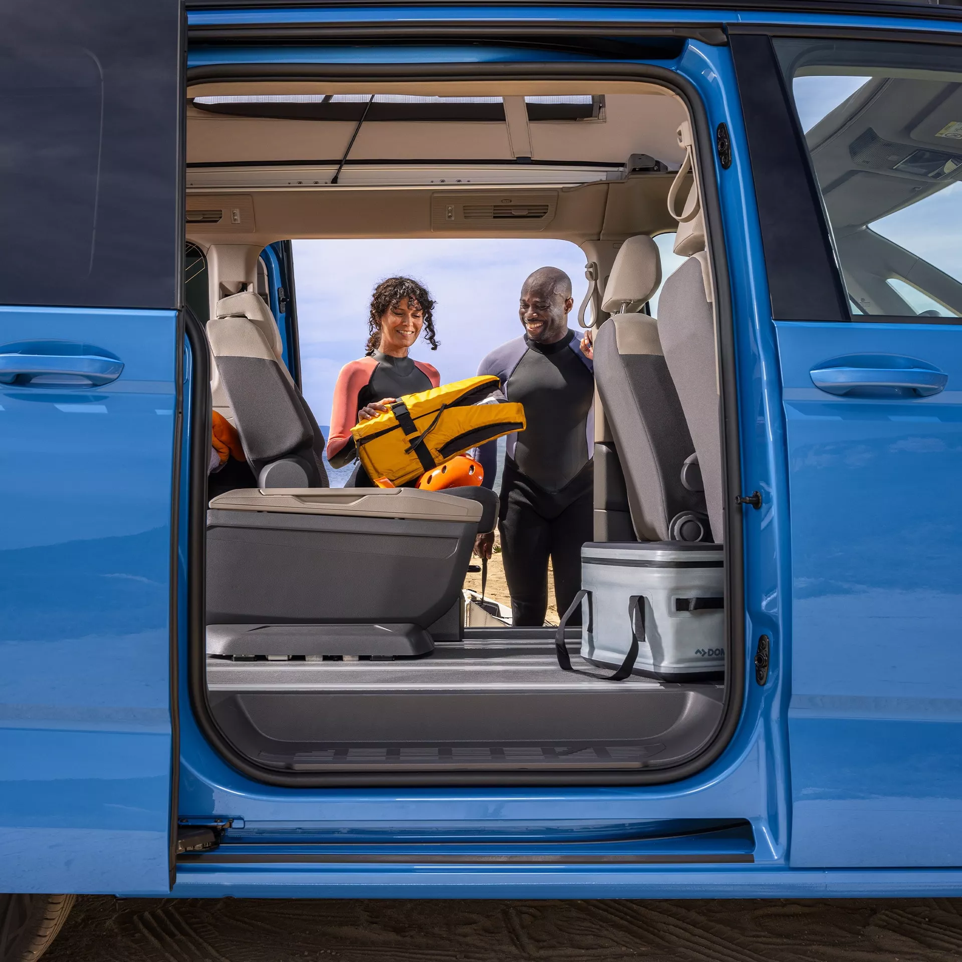 Due persone sorridenti in tenuta da surf dall'interno di un furgone blu.