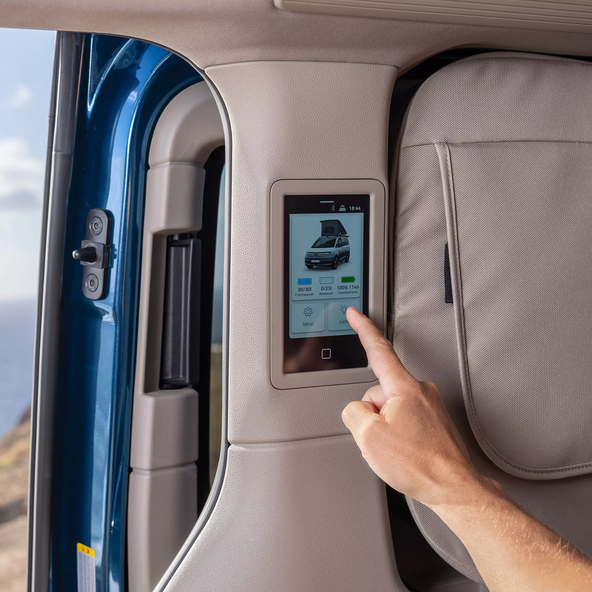 Un dito preme un touchscreen a bordo di un camper che mostra i livelli dell'acqua e della batteria.