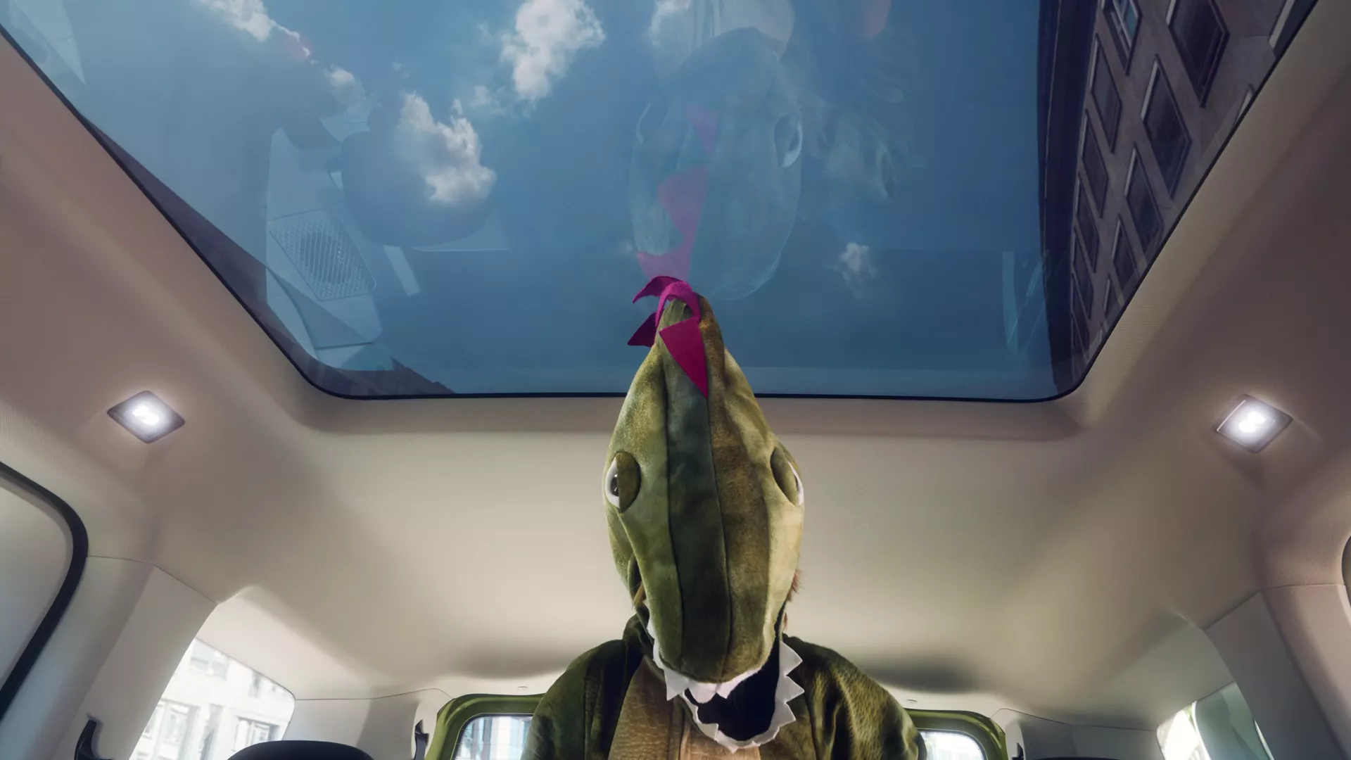 Vista interna di un passeggero con indosso un costume da dinosauro in macchina.