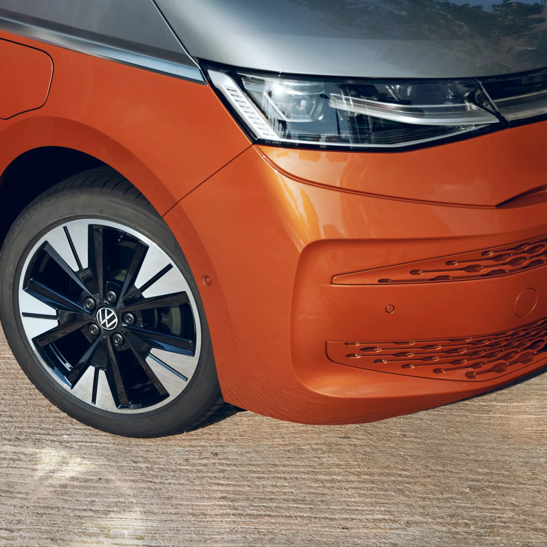 Primo piano della parte anteriore di un furgone arancione e grigio Volkswagen ID. Buzz, che mostra il faro, la ruota e la paraurti.