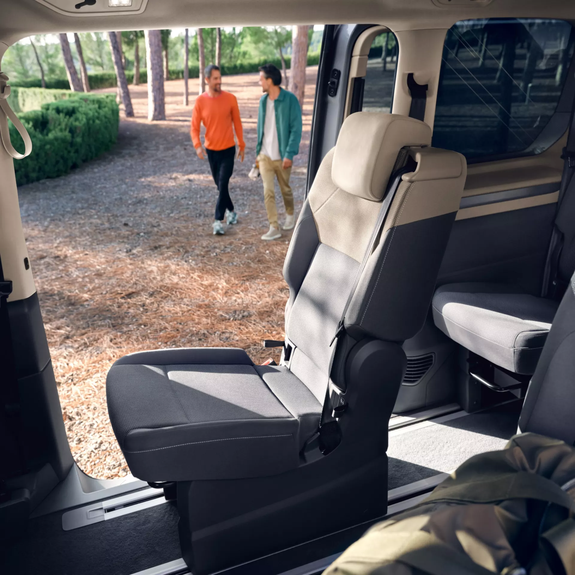 Interni di un'auto con sedili grigi e beige. Due persone camminano fuori.