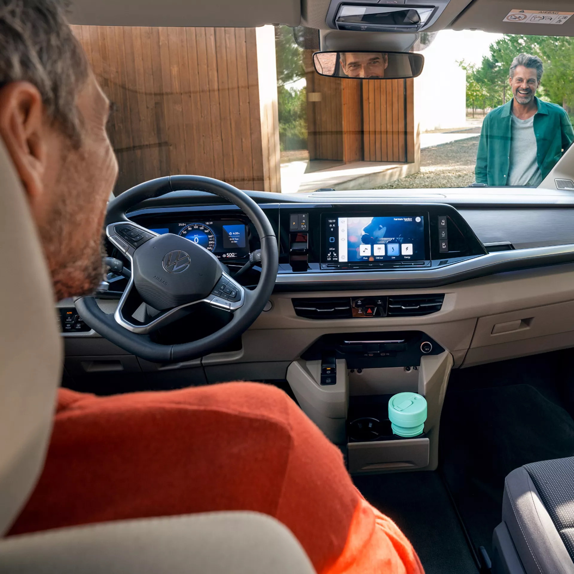 L'interno elegante e moderno del veicolo Volkswagen è esaltato da un uomo sorridente nello specchietto retrovisore e da una tazza verde menta.