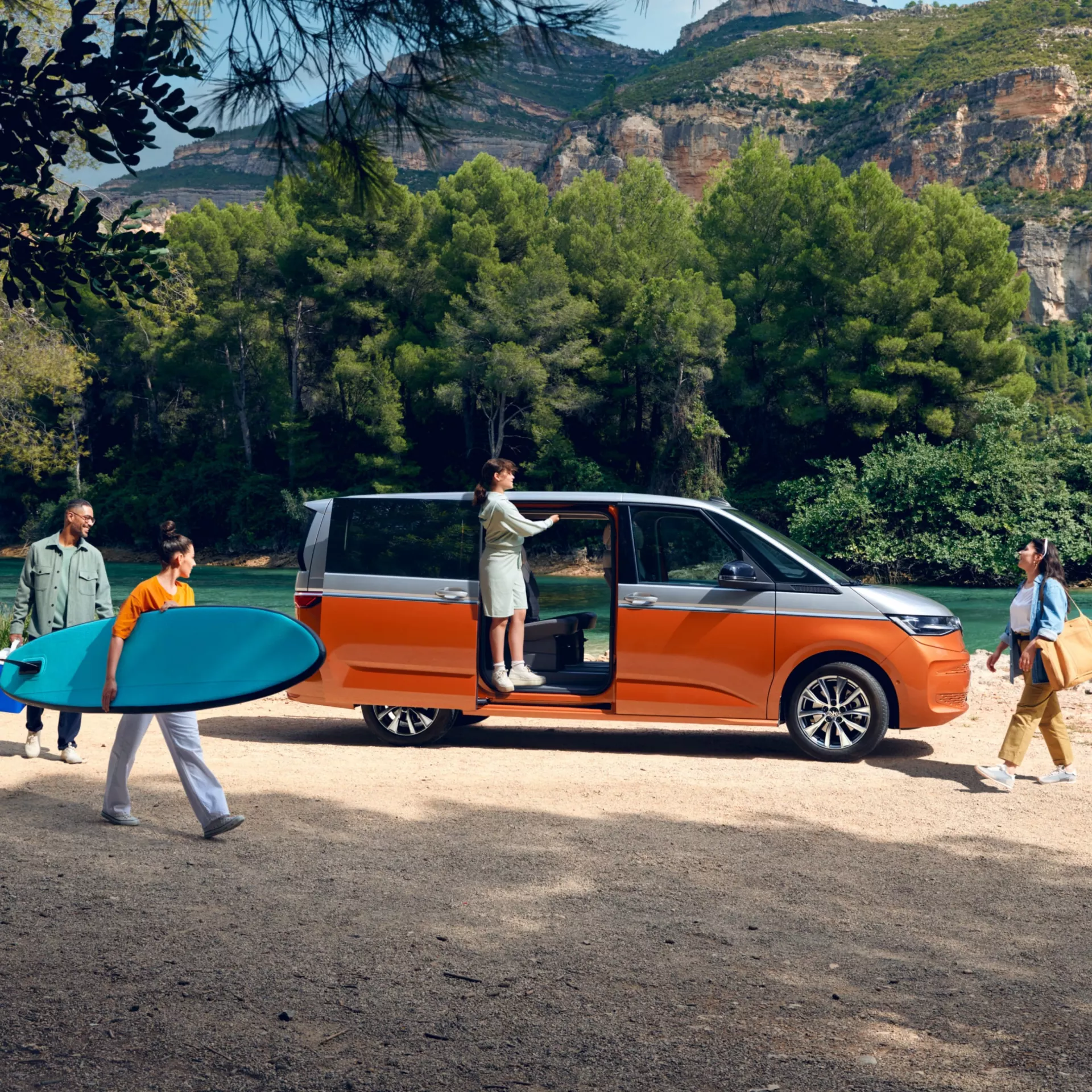 Un gruppo di persone accanto a un furgone arancione vicino a un lago con una tavola da surf.