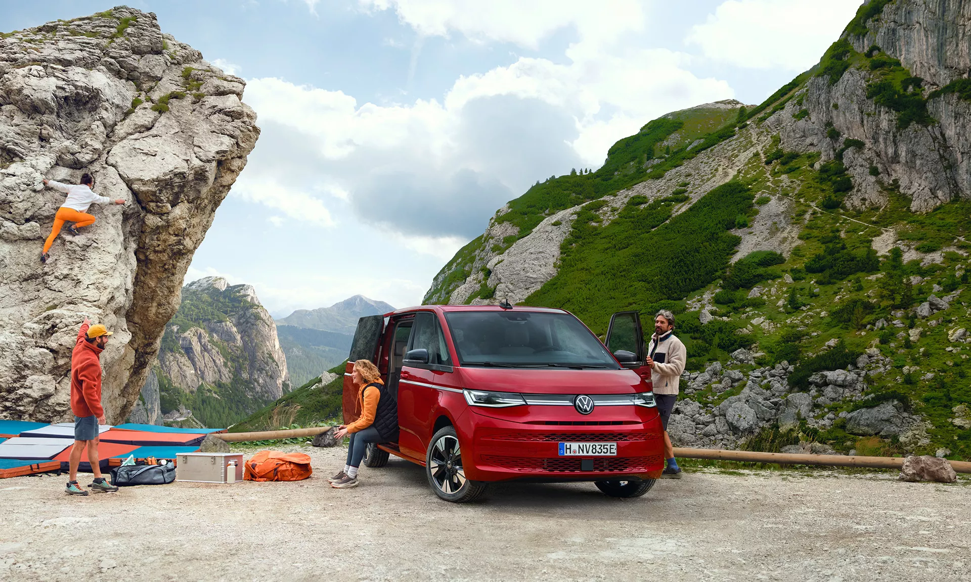 Persone che si preparano a fare arrampicata su roccia vicino a un furgone Volkswagen rosso.