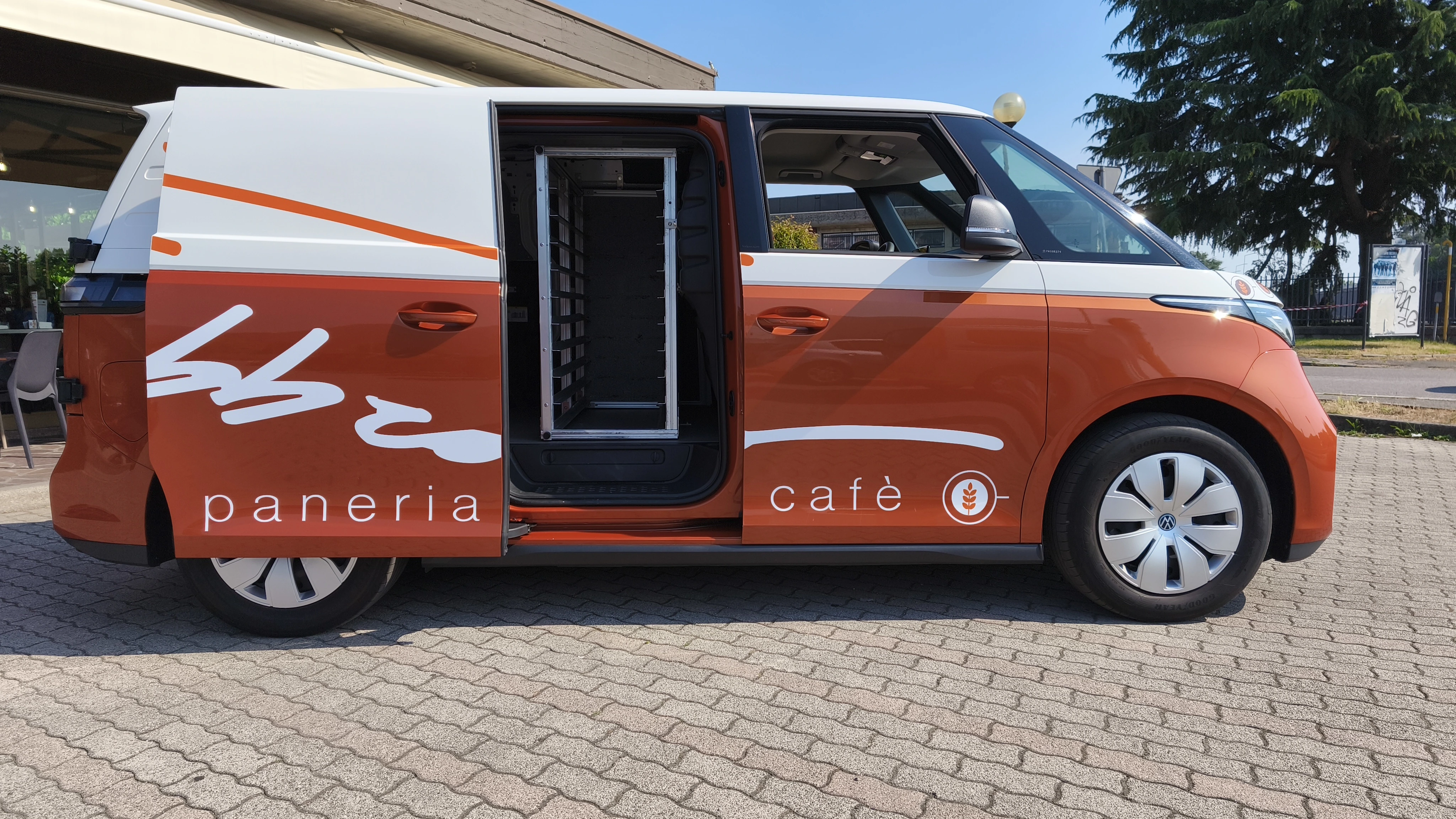 Volkswagen ID. Buzz, furgone elettrico a due tonalità arancione e bianco, con la scritta "paneria café" sul lato.