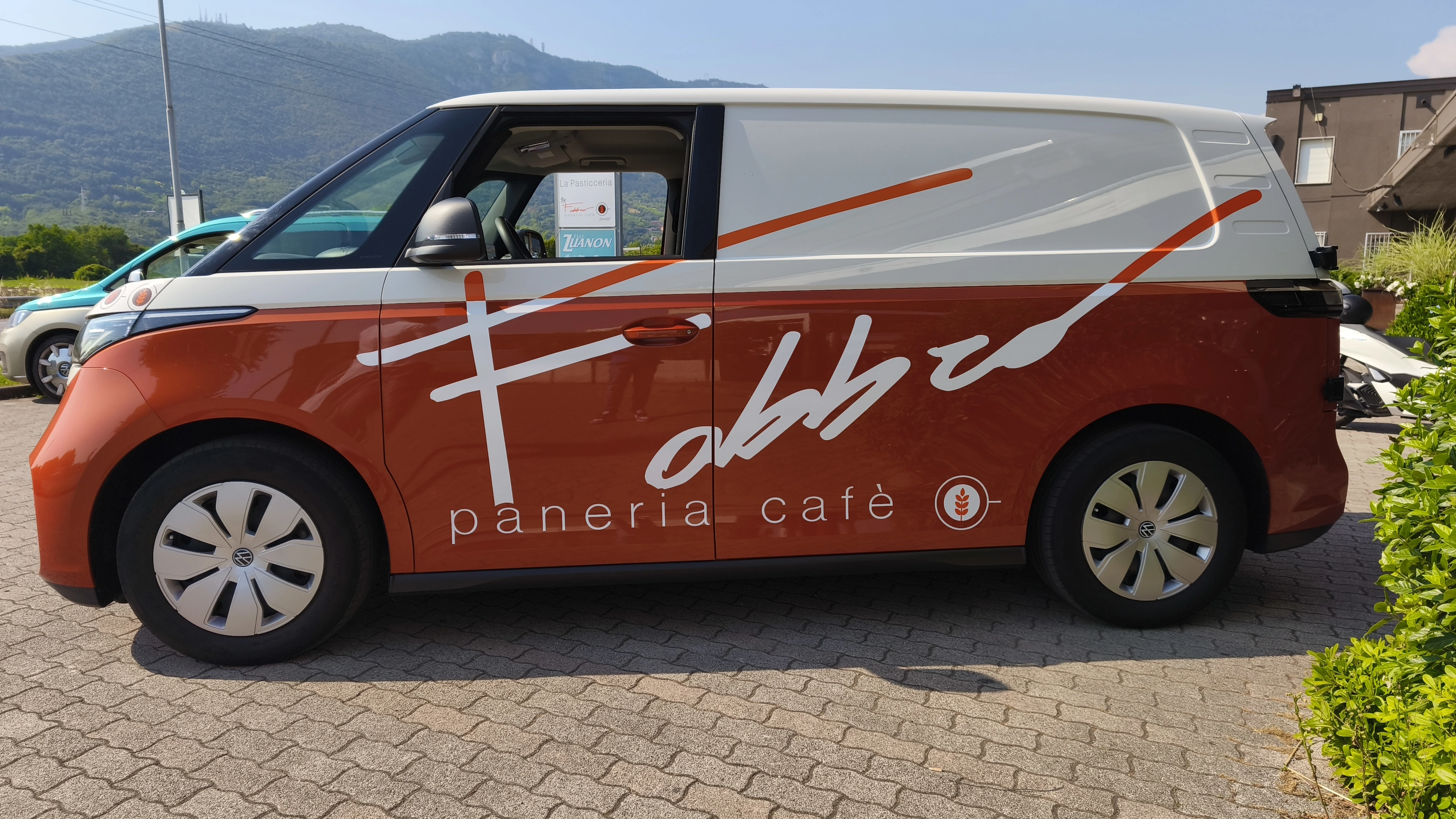 Un furgone Volkswagen ID. Buzz color arancione e bianco parcheggiato con il logo di una panetteria.