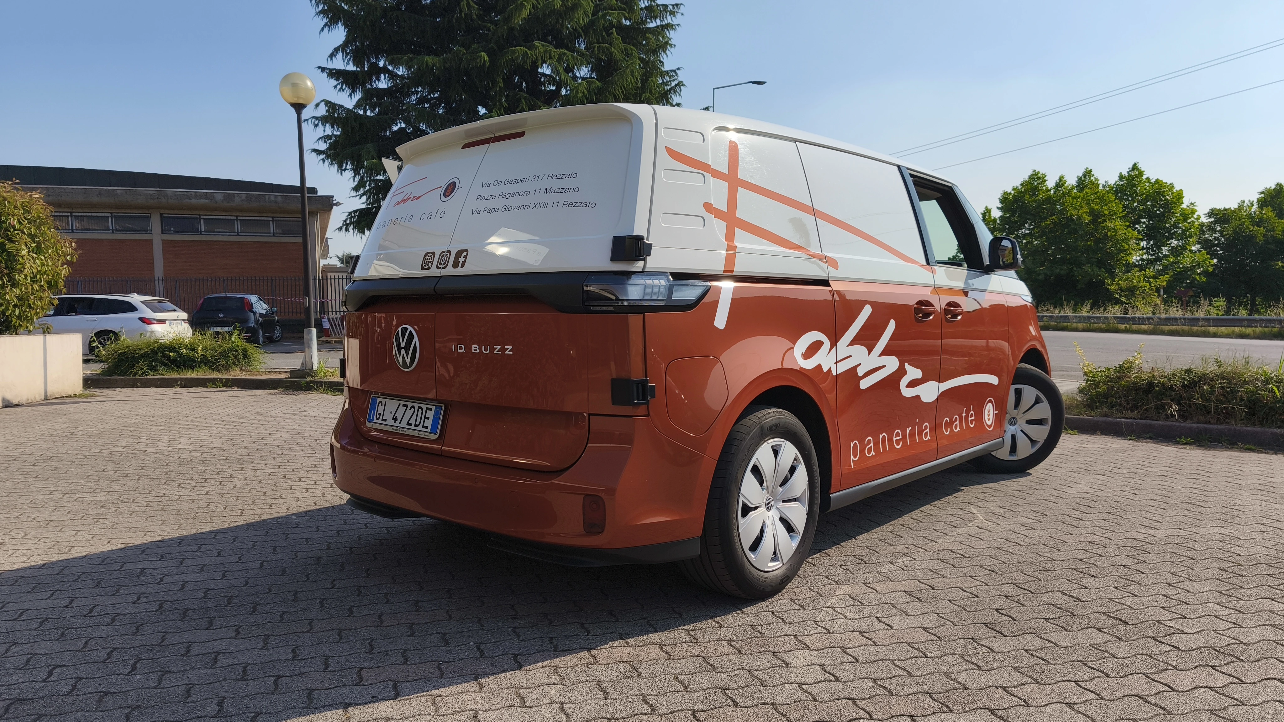 Furgone Volkswagen ID.Buzz arancione e bianco, pubblicizza una panetteria-caffetteria italiana.