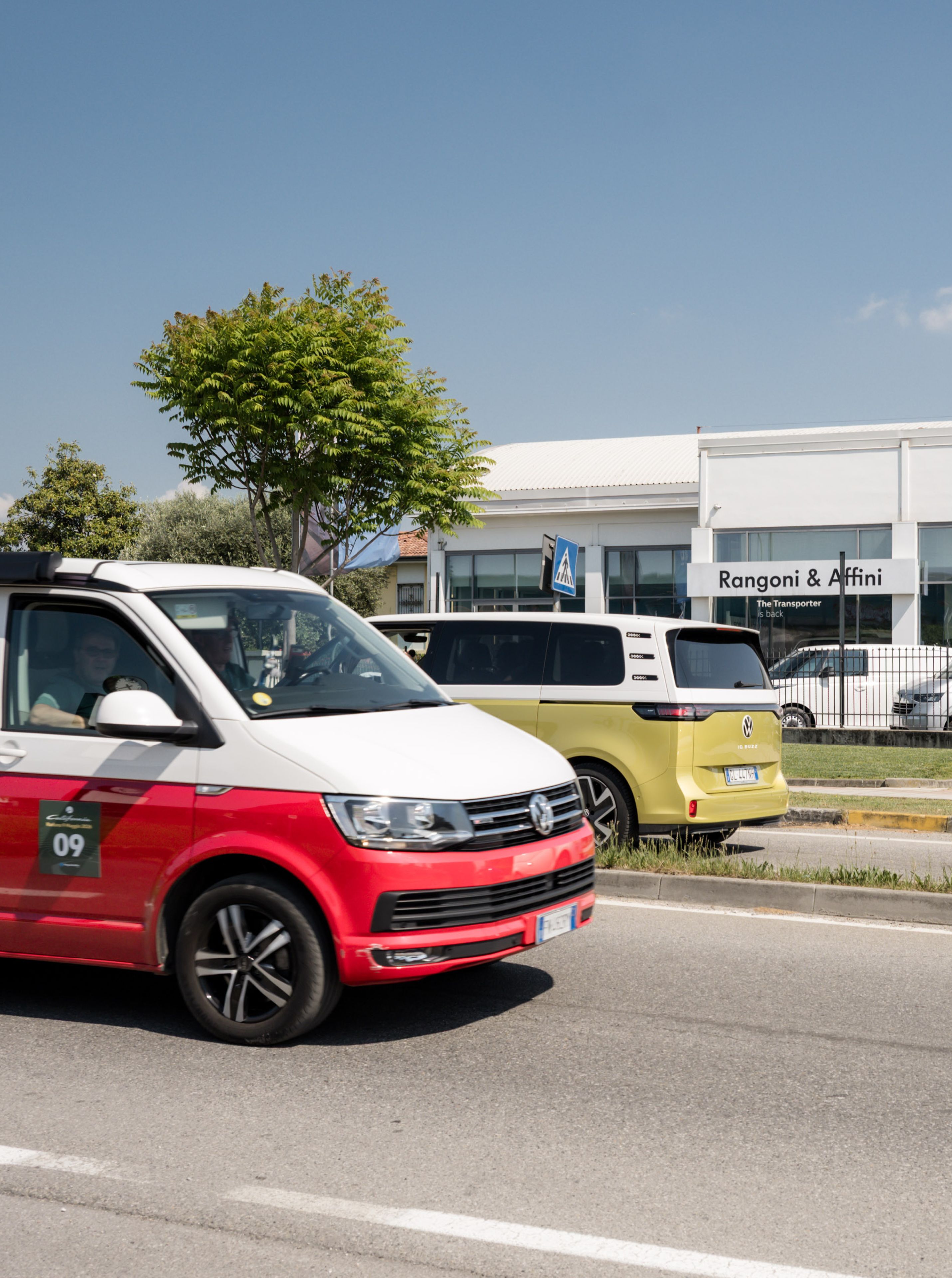 Una California rossa e bianca passa davanti a una ID. Buzz gialla e una Fiat 500 parcheggiate presso la concessionaria VW.