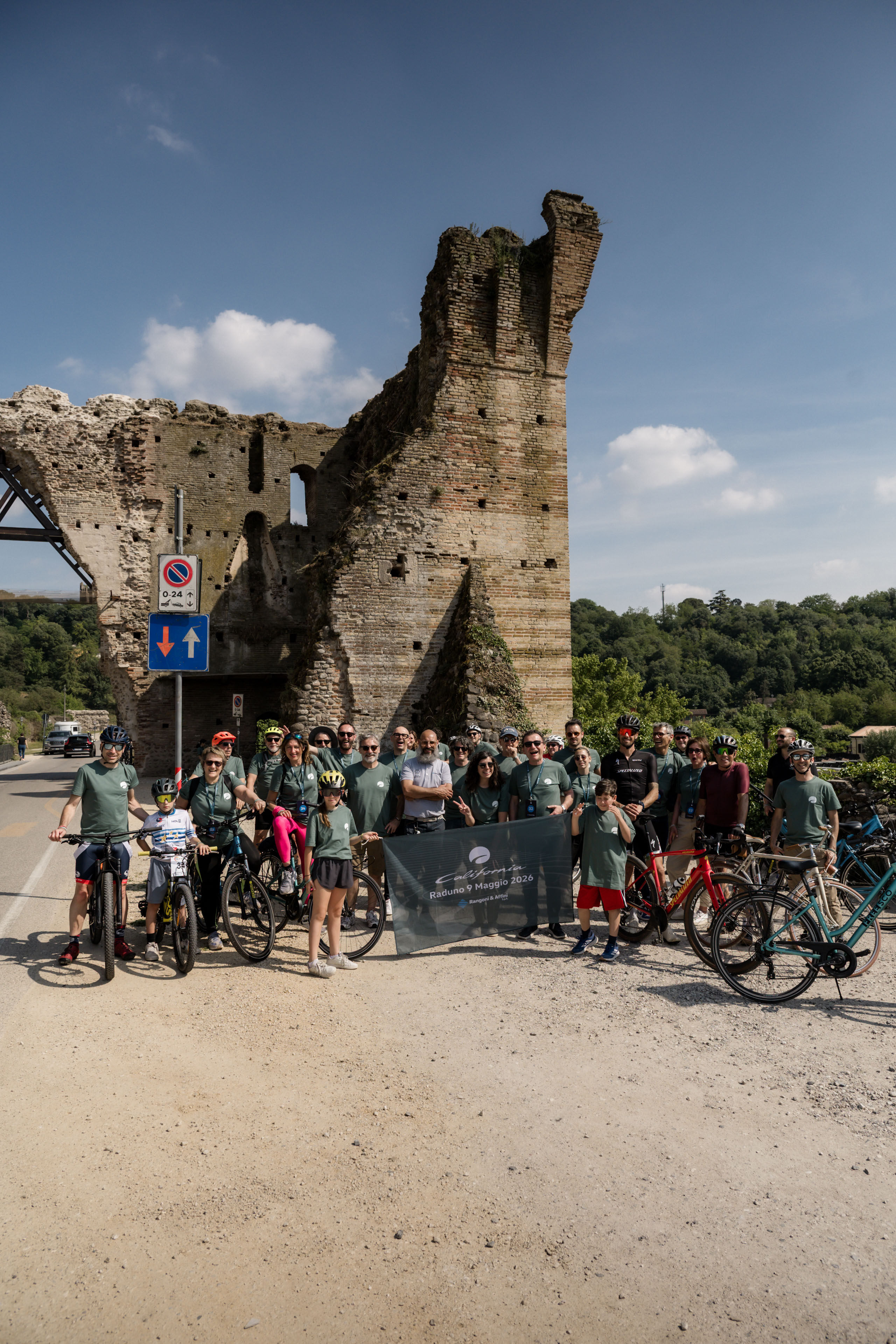 Ciclisti sorridenti al Raduno 9 Maggio 2026 davanti a suggestive rovine storiche.