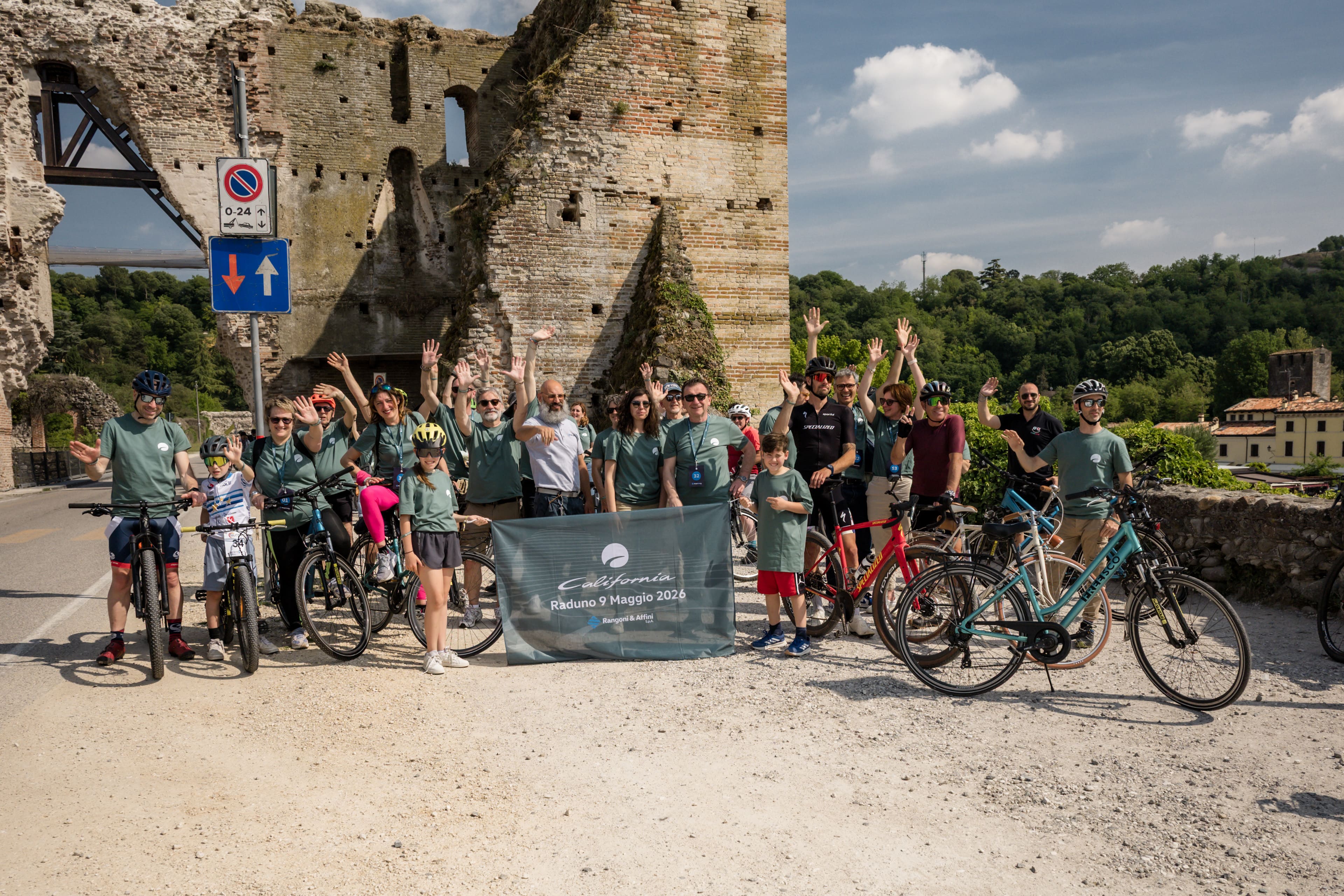 bike-experience-borghetto.jpg Amici in mountain bike celebrano e scattano selfie in un incredibile paesaggio alpino con fiume e sole.