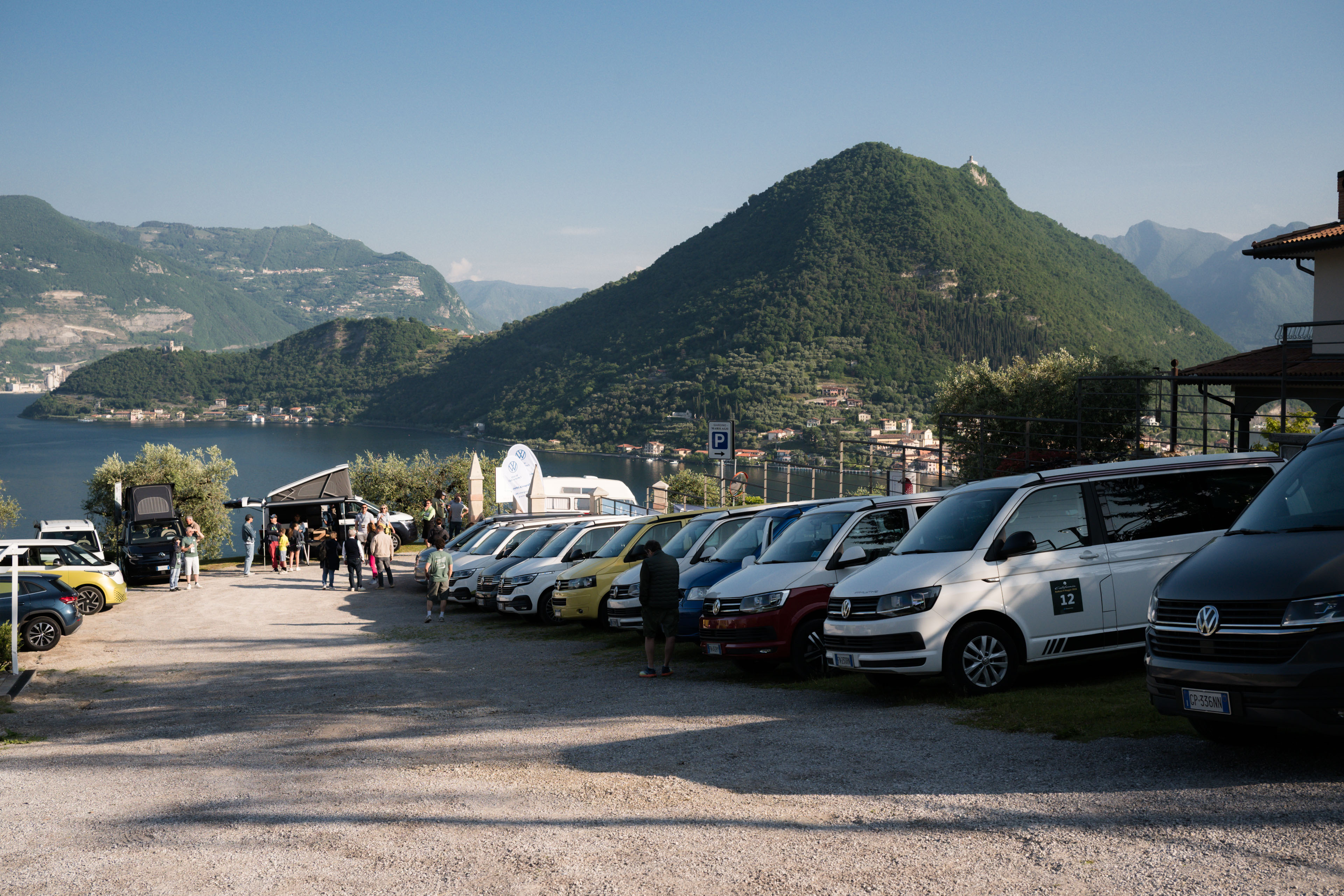 california-lago-iseo.jpg Camper con tetto a soffietto in un parcheggio panoramico. Vista mozzafiato su lago e montagne.