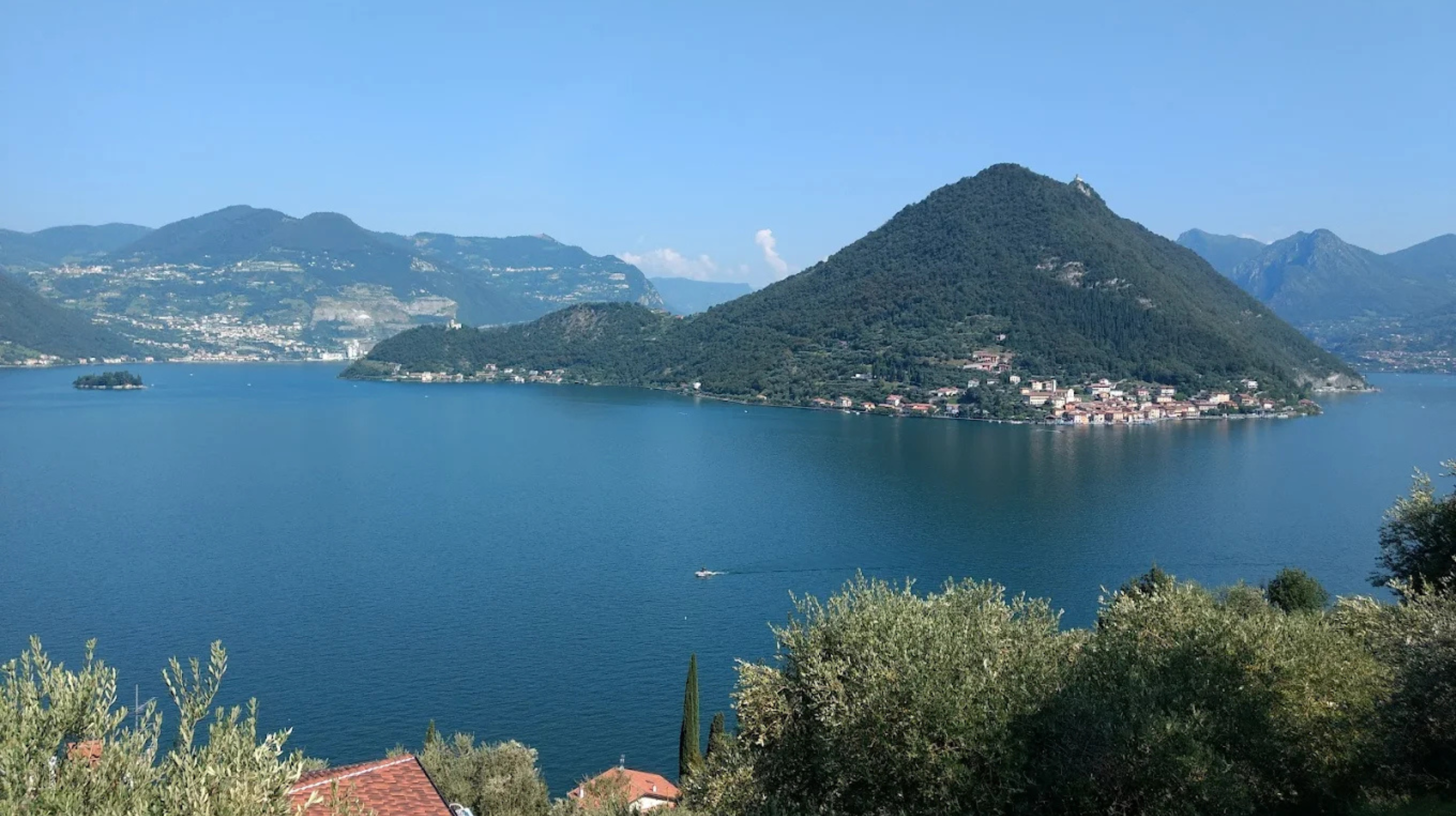 Paesaggio lacustre mozzafiato: acque blu, montagne rigogliose e un borgo incantevole sotto un cielo sereno.