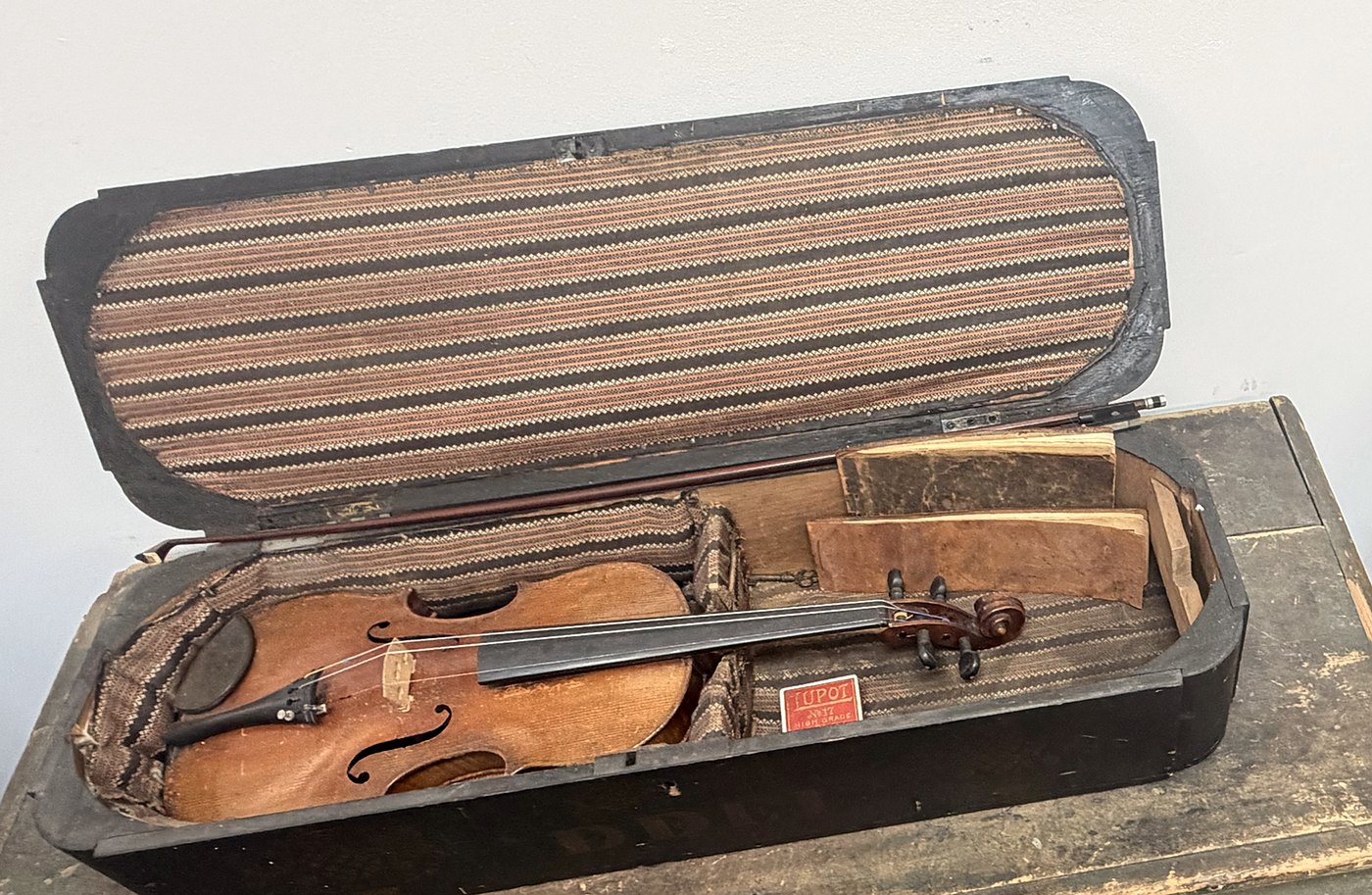 A violin and bow in an open wooden case lined with striped cloth