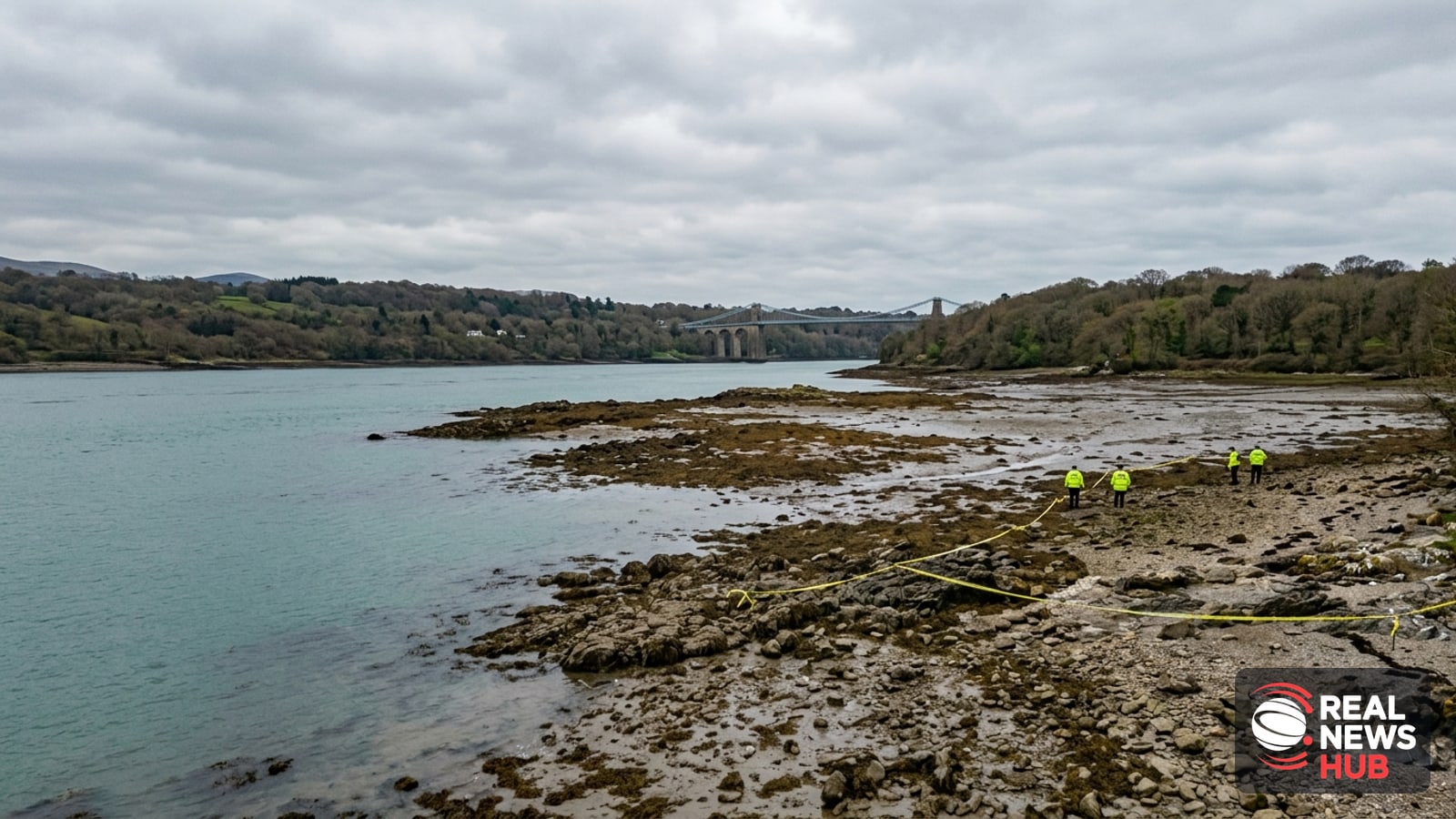 Aerial view of a rocky shoreline near the Menai strait in north Wales with police tape and distant officers conducting a search.