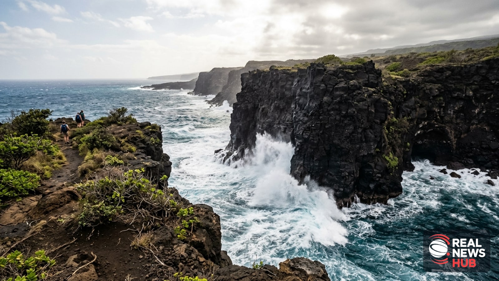 Craggy black basalt sea cliffs in Hawaii battered by surging white Pacific waves under a hazy tropical sky.