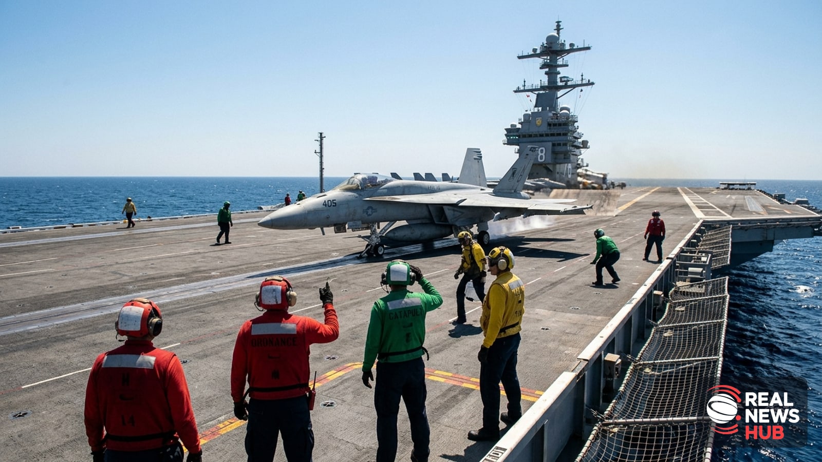 U.S. Navy flight deck crew in protective gear watch a fighter jet prepare for takeoff on an aircraft carrier at sea under bright sunlight.