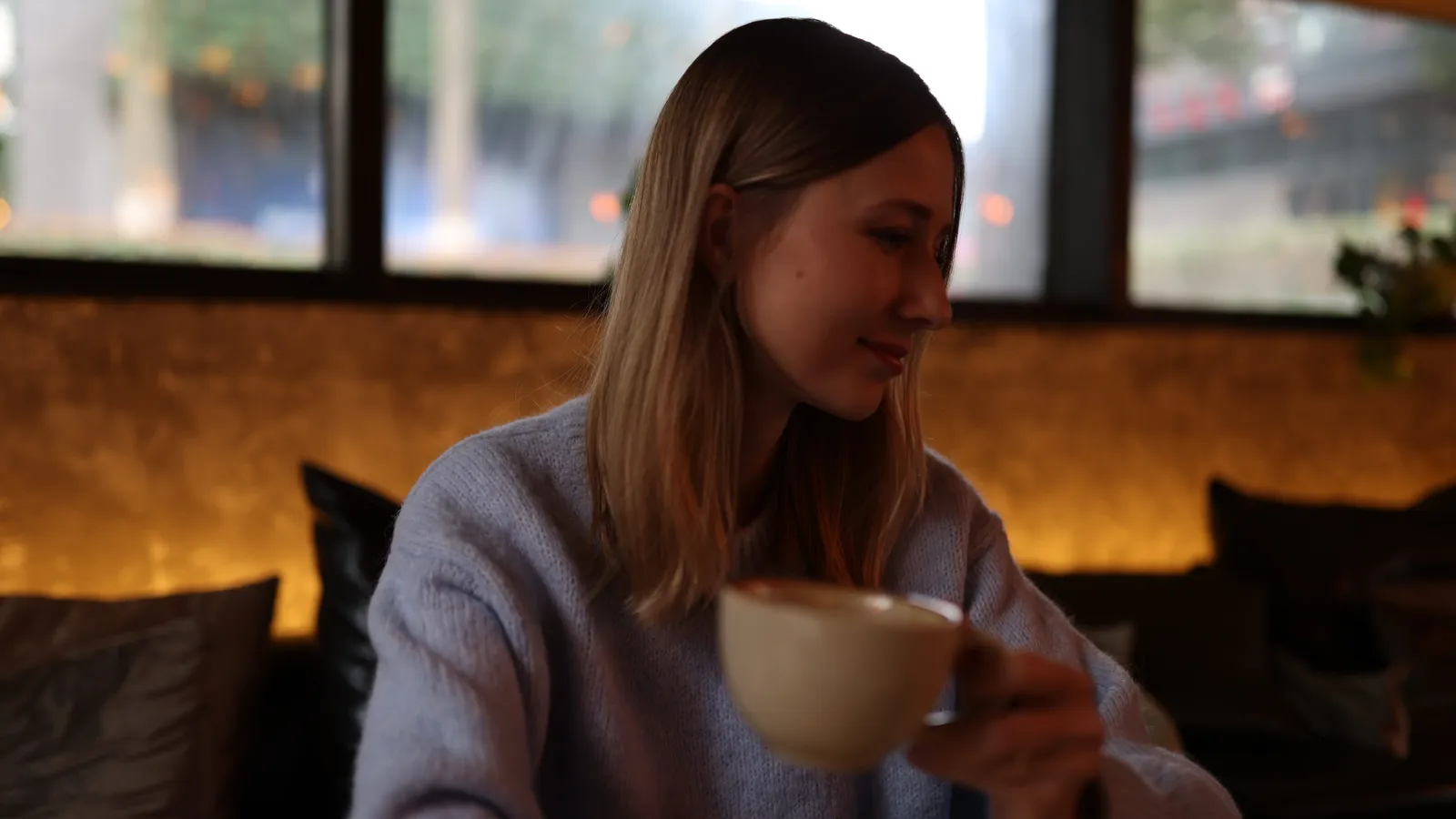 Woman drinking coffee at a cafe table by a window
