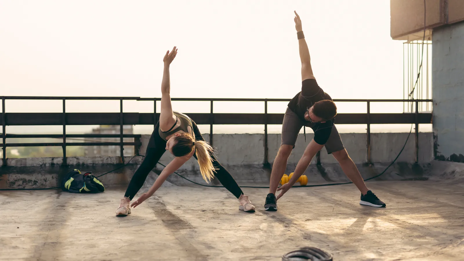 Two people stretching side by side on a rooftop terrace