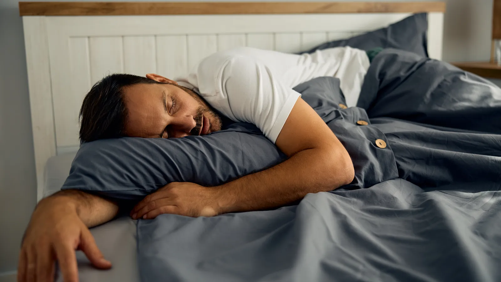 Man asleep on his front in bed, one arm resting over the duvet