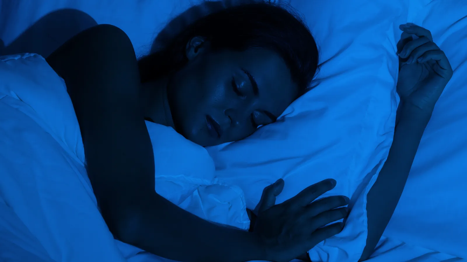 Woman asleep in bed at night under blue light