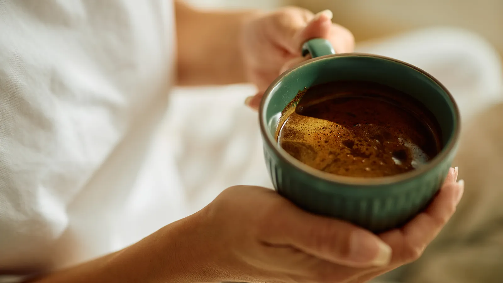 Hands holding a cup of fresh coffee in bed in the morning