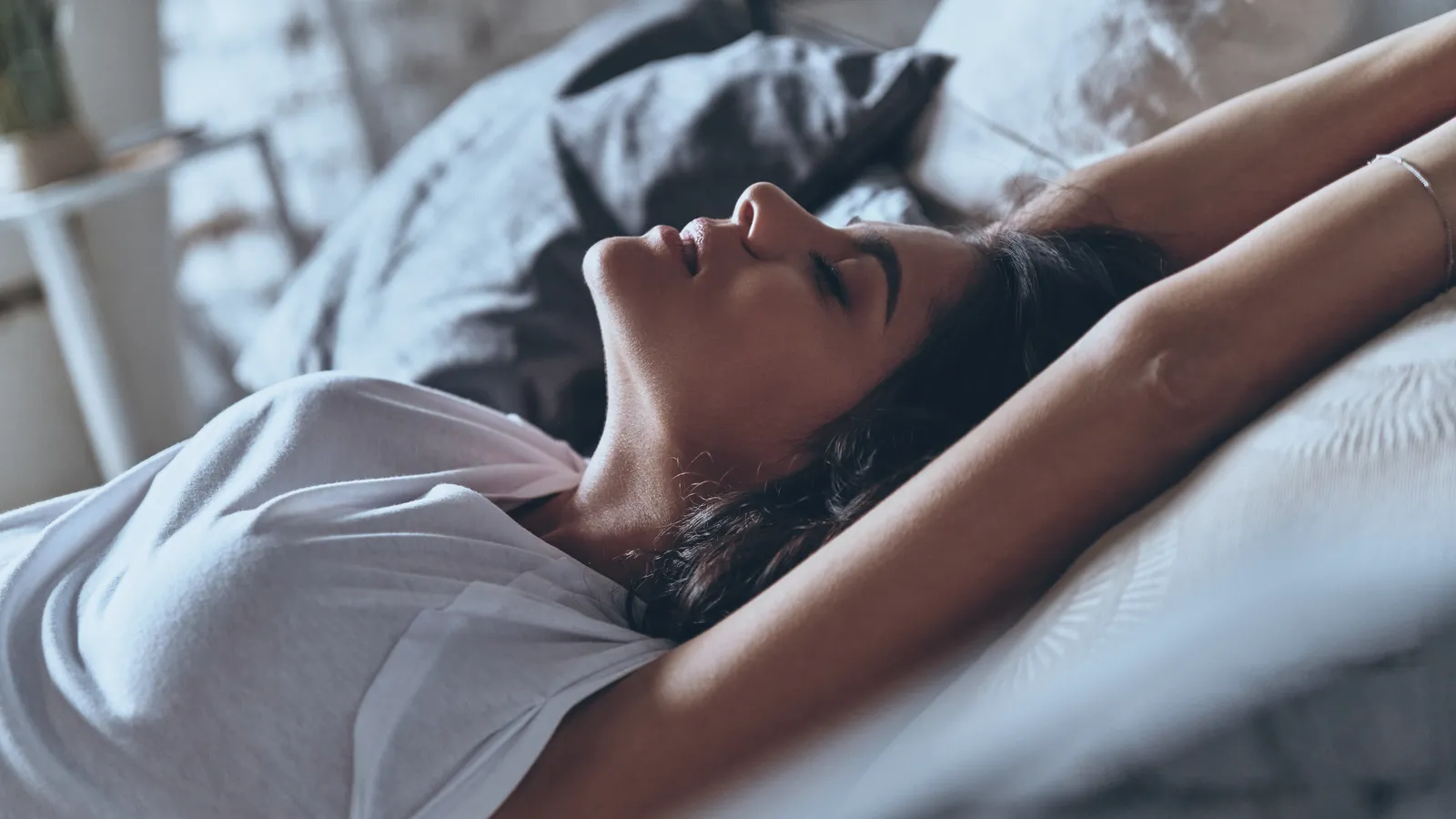 Woman resting in bed in the morning light, covers pulled up