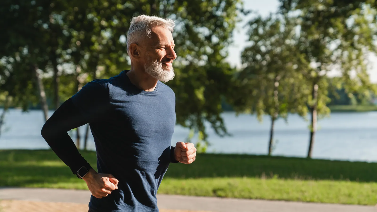 Mature male athlete running outdoors along a lakeside path