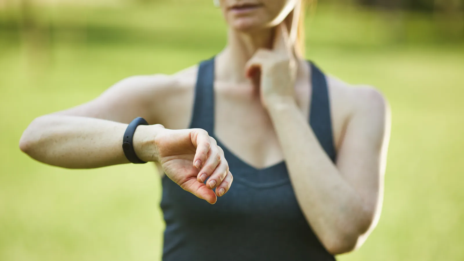Woman outdoors checking the fitness tracker on her wrist while taking her pulse