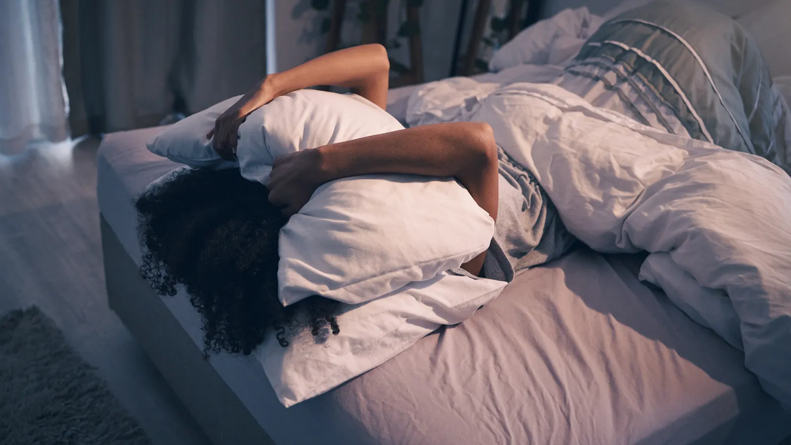 Person lying face down in bed with a pillow pulled over their head
