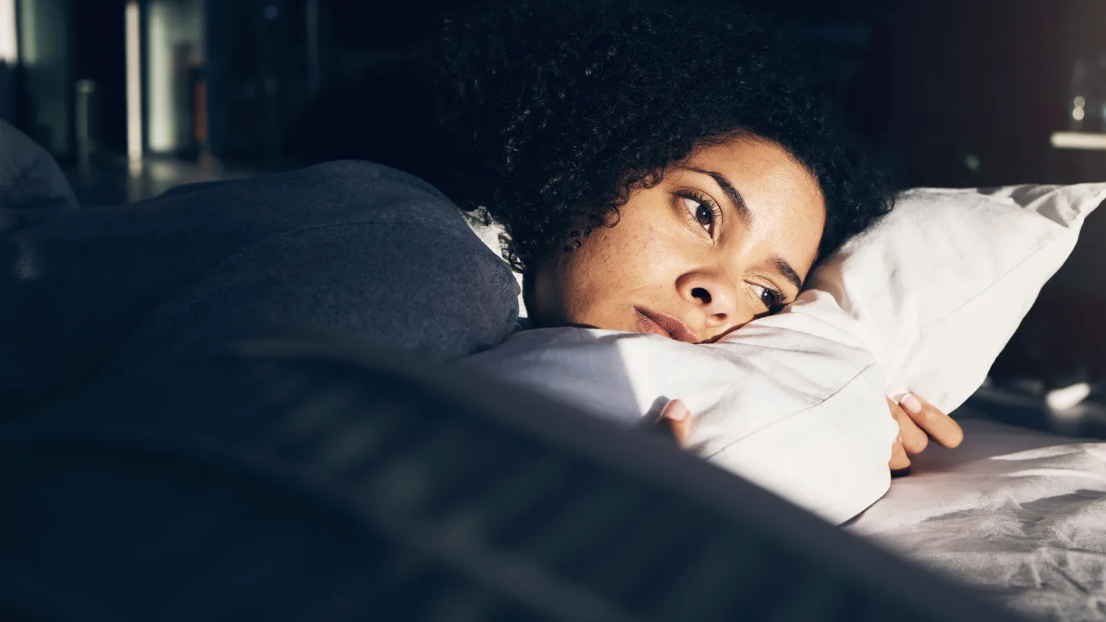Woman lying awake in bed in early morning light, eyes open