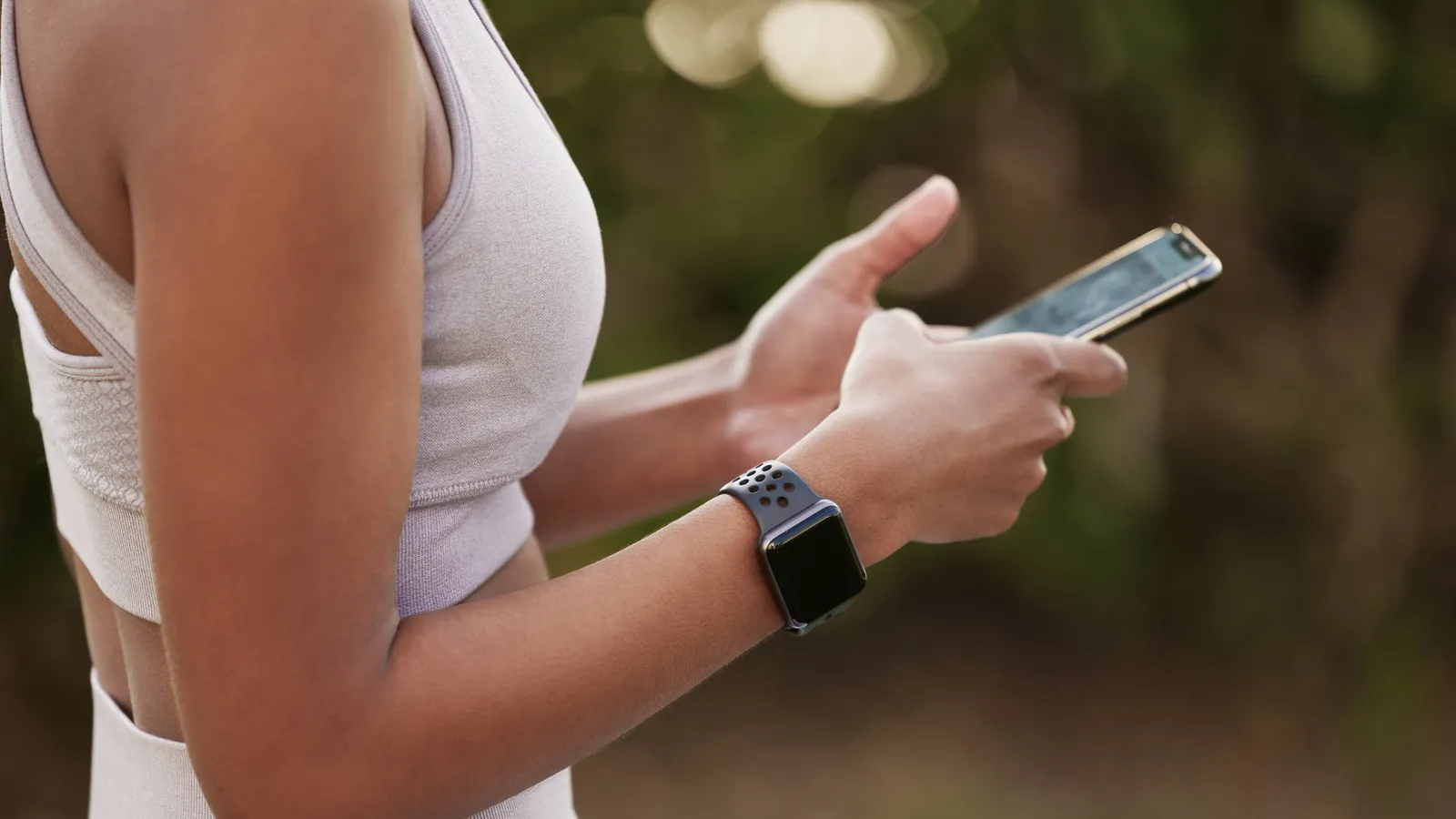 Woman in athletic wear outdoors checking her phone, a smartwatch on her wrist