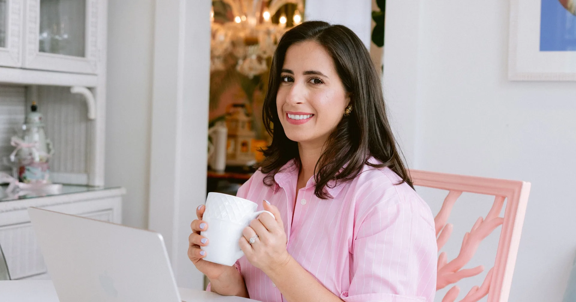 Natalie Sterling smiling with a coffee mug at her laptop in a bright white kitchen