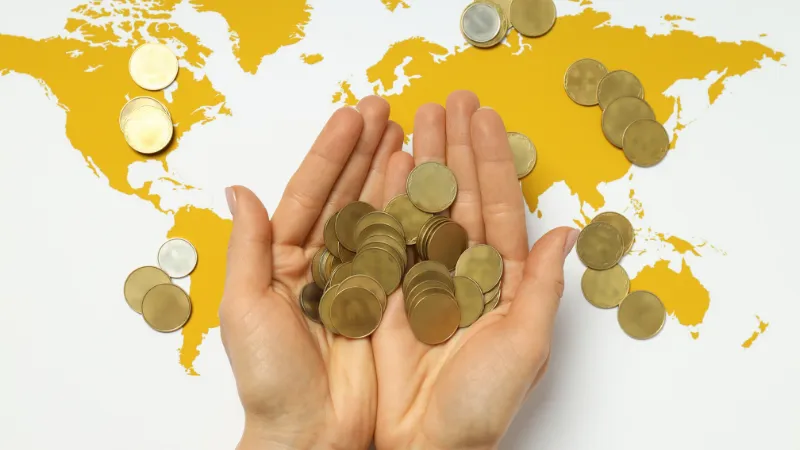 unas manos sosteniendo monedas con un planisferio detras, simbolizan la independencia económica
