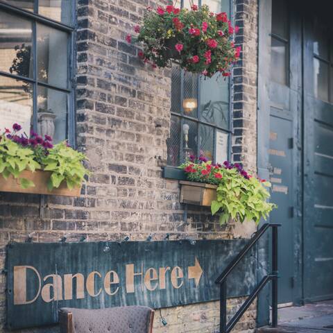 Photo of a building from an alley with a 'dance here' sign pointed towards the door.