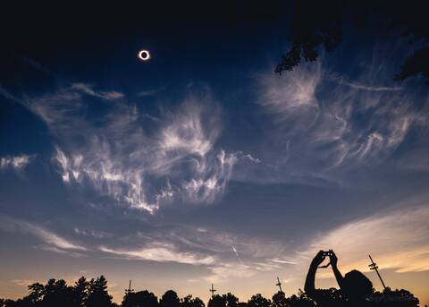 A solar eclipse in the sky, silhouette of people visible in the foreground