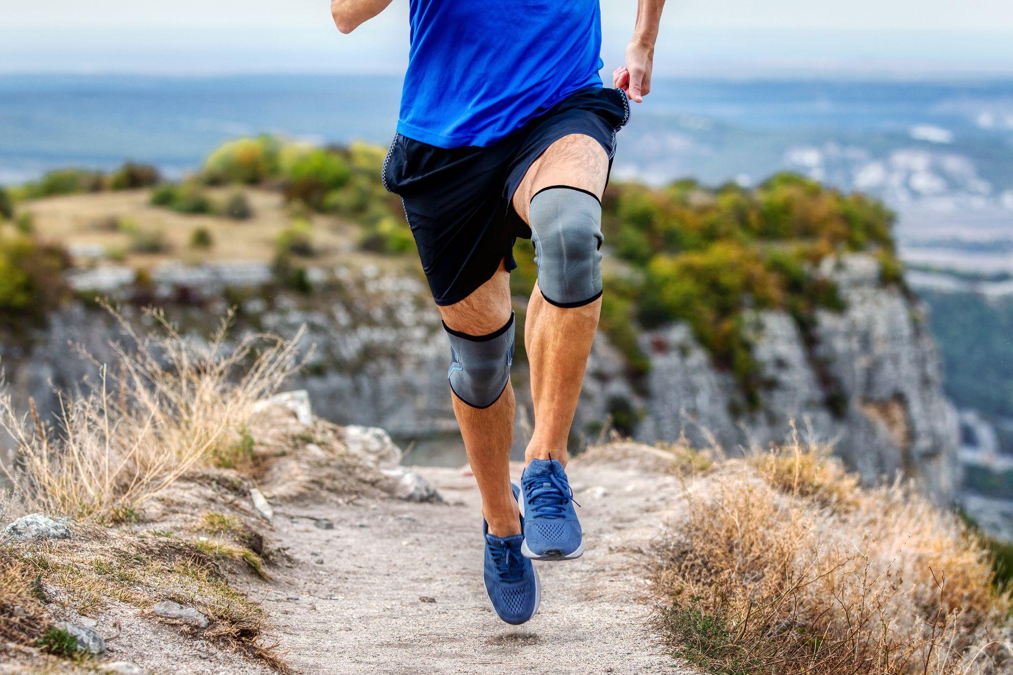 A man running in the mountains wearing knee caps and good-fitted shoes for safety.