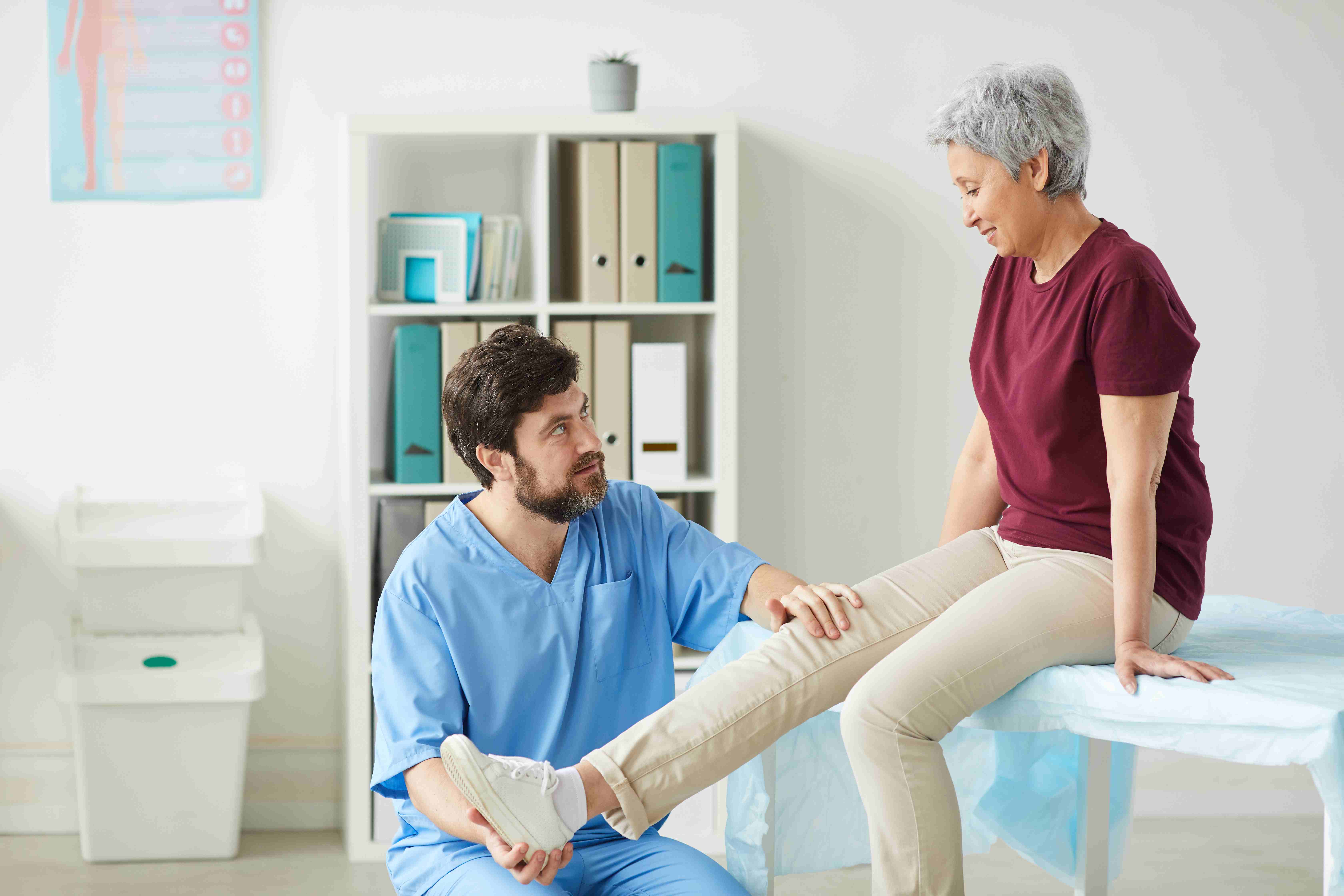 Doctor examining the leg of a senior woman during a consultation for potential knee replacement surgery.