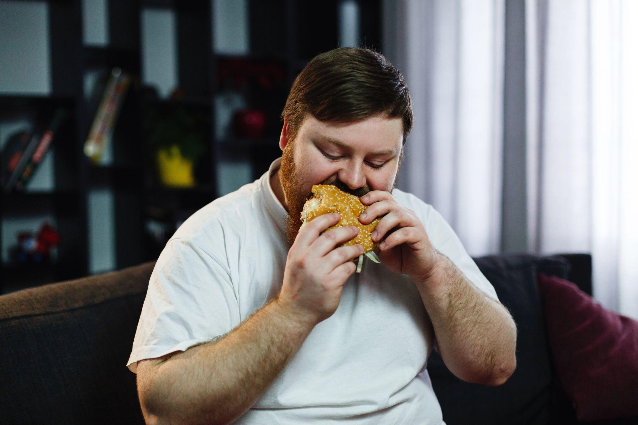 Overweight man eating burger while sitting at home