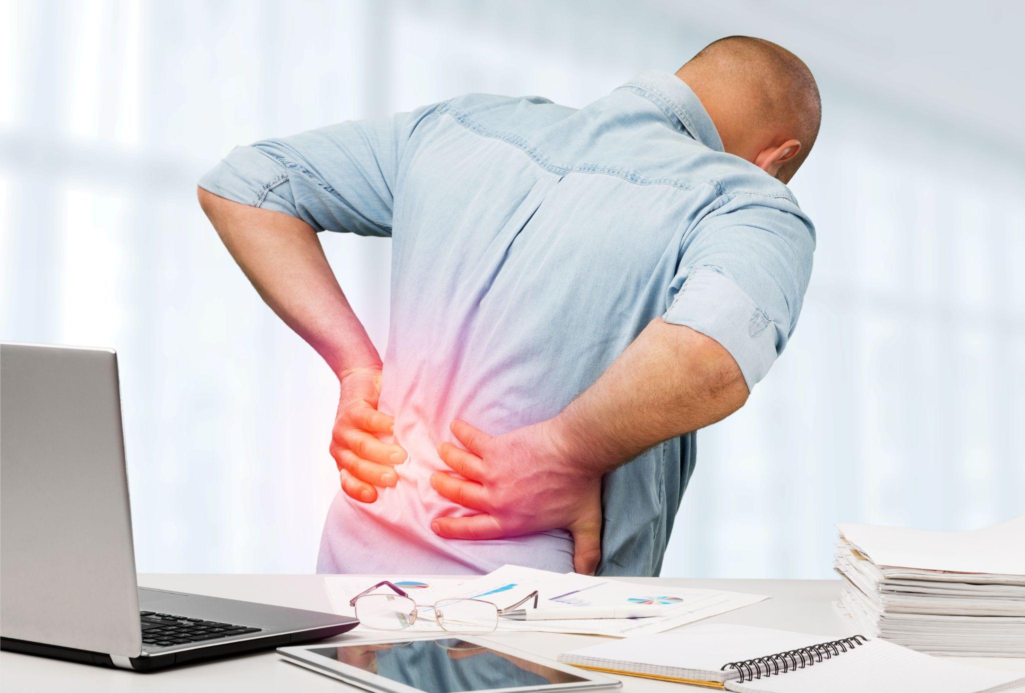 An office worker suffering from back pain, illustrating work-related posture issues and prolonged sitting causing spinal discomfort.