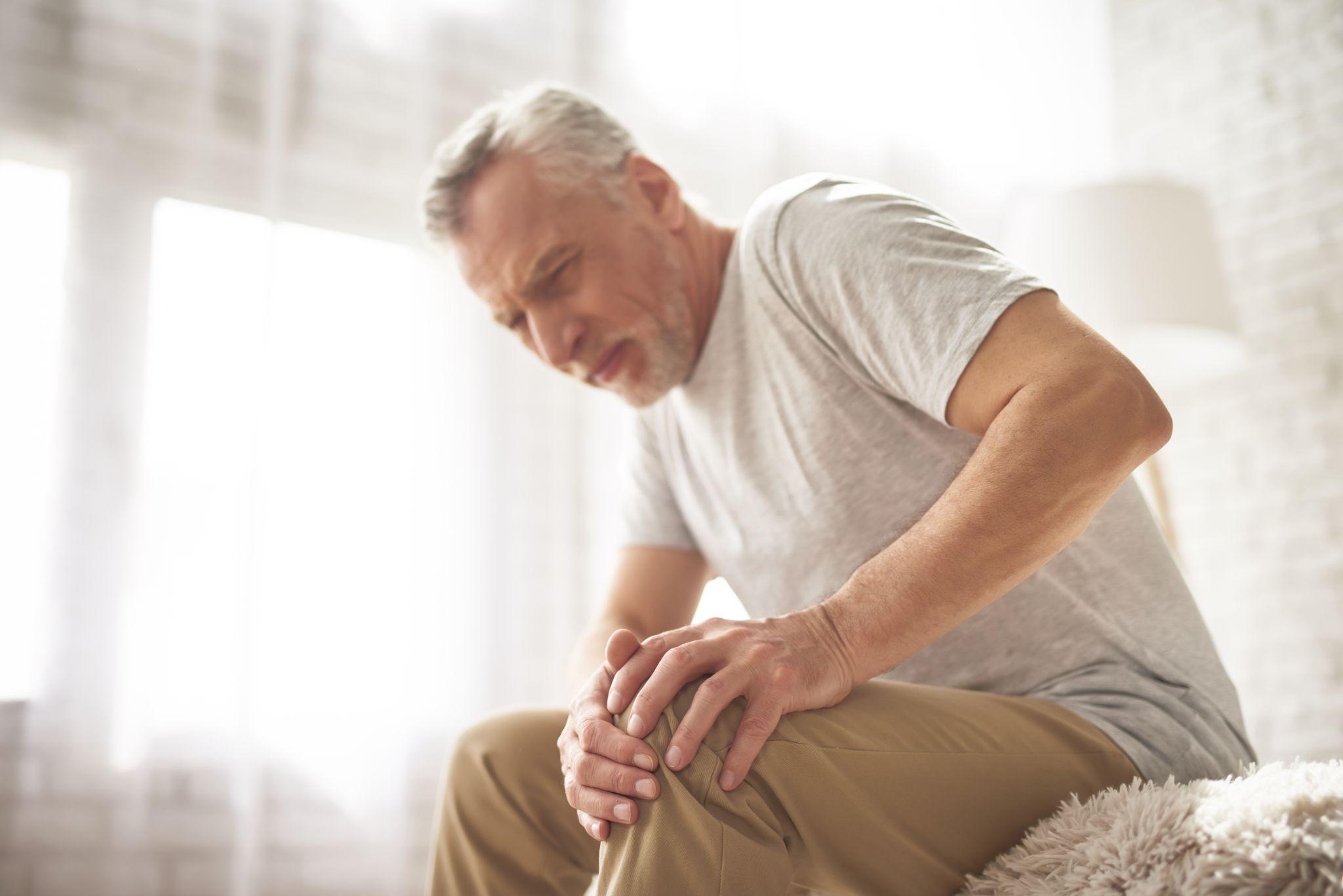 An elderly man holding his knee at home, representing age-related joint pain and early signs of osteoarthritis.
