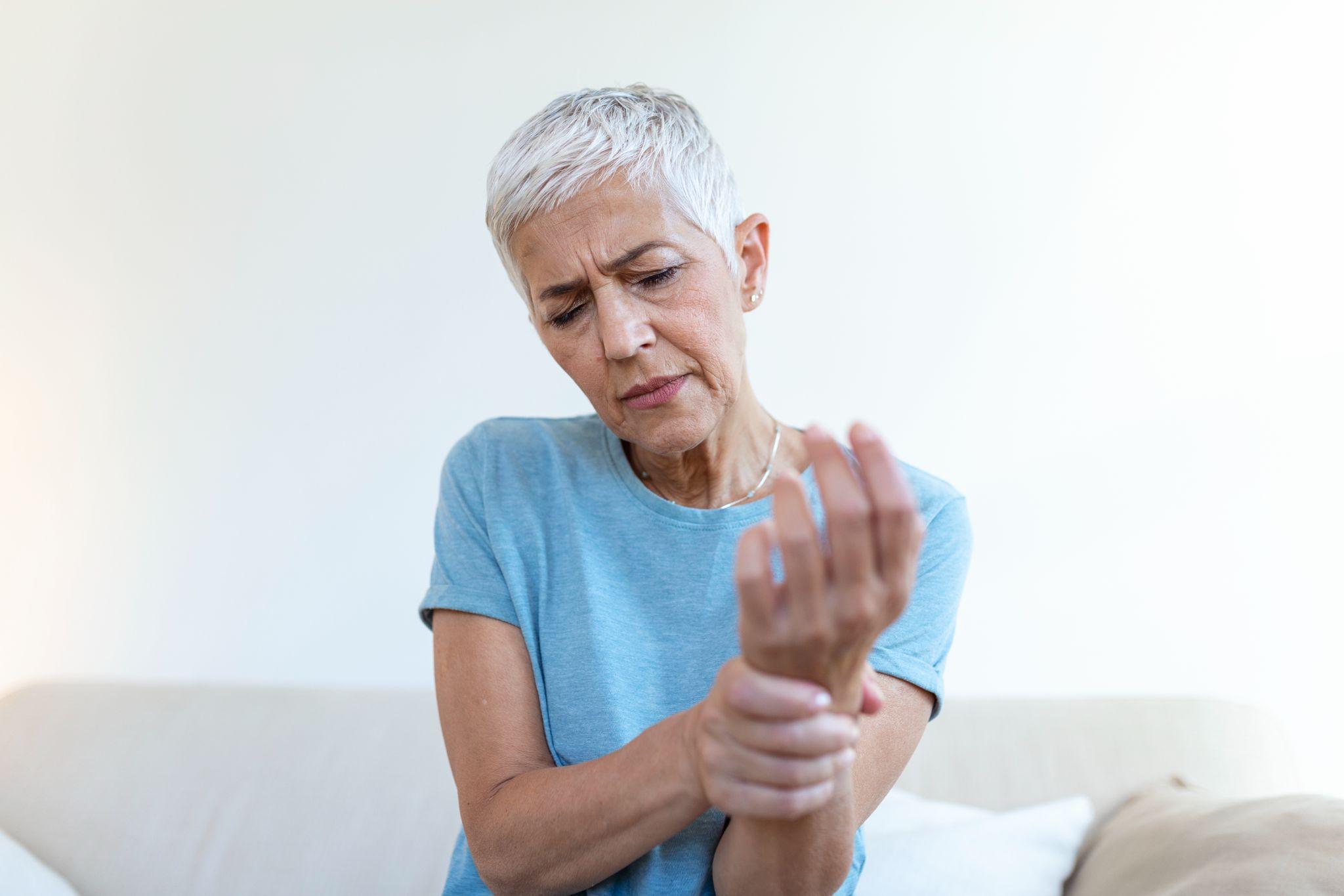 A senior woman experiencing hand joint pain, indicating arthritis-related stiffness and age-associated joint degeneration.