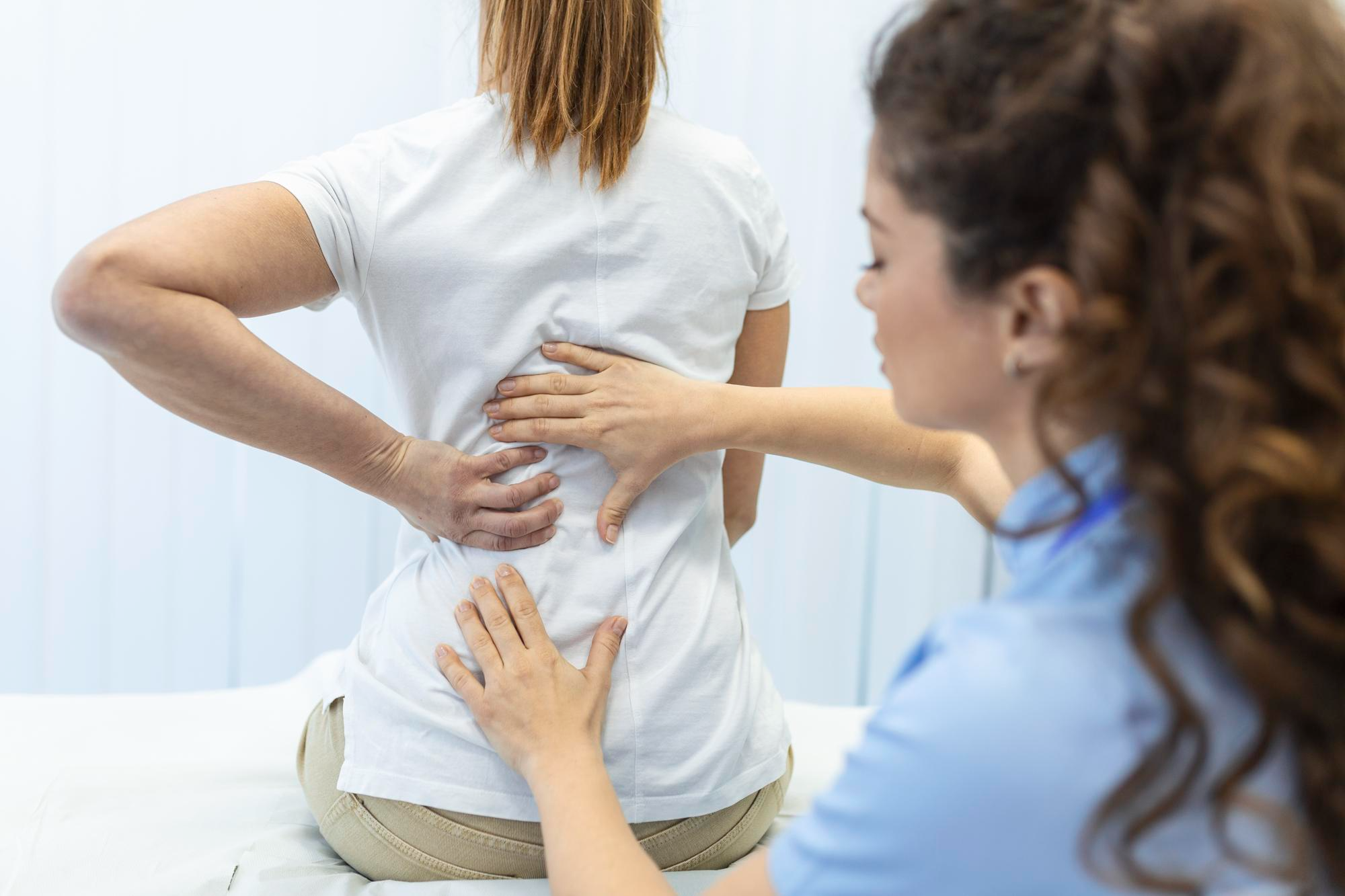 A professional clinical scene showing a woman discussing her symptoms with a doctor during a medical consultation, highlighting the importance of timely diagnosis and expert care for managing back pain and related conditions.