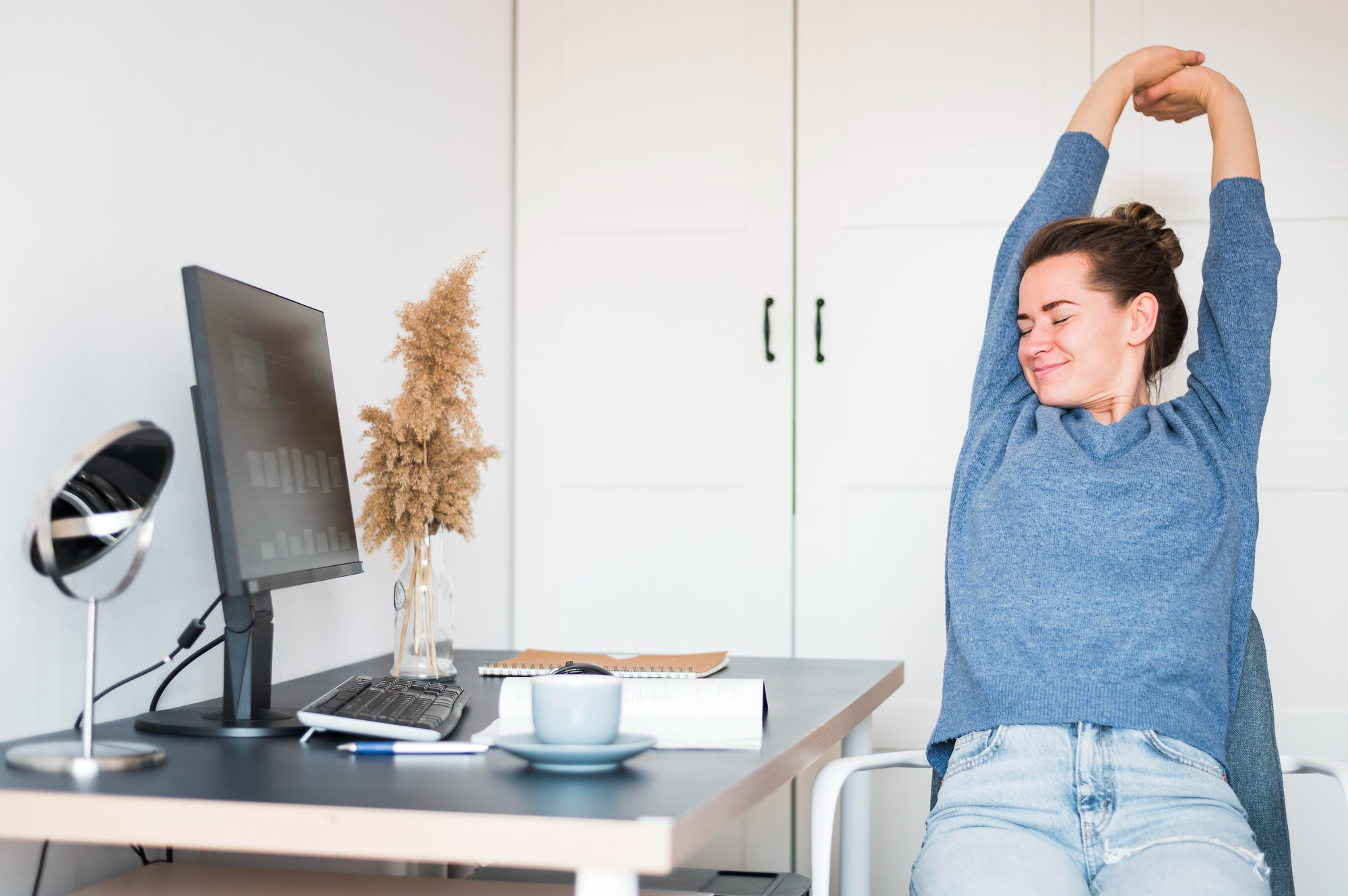 A woman pausing from desk work to stretch, reinforcing the need for regular movement to support spinal health.