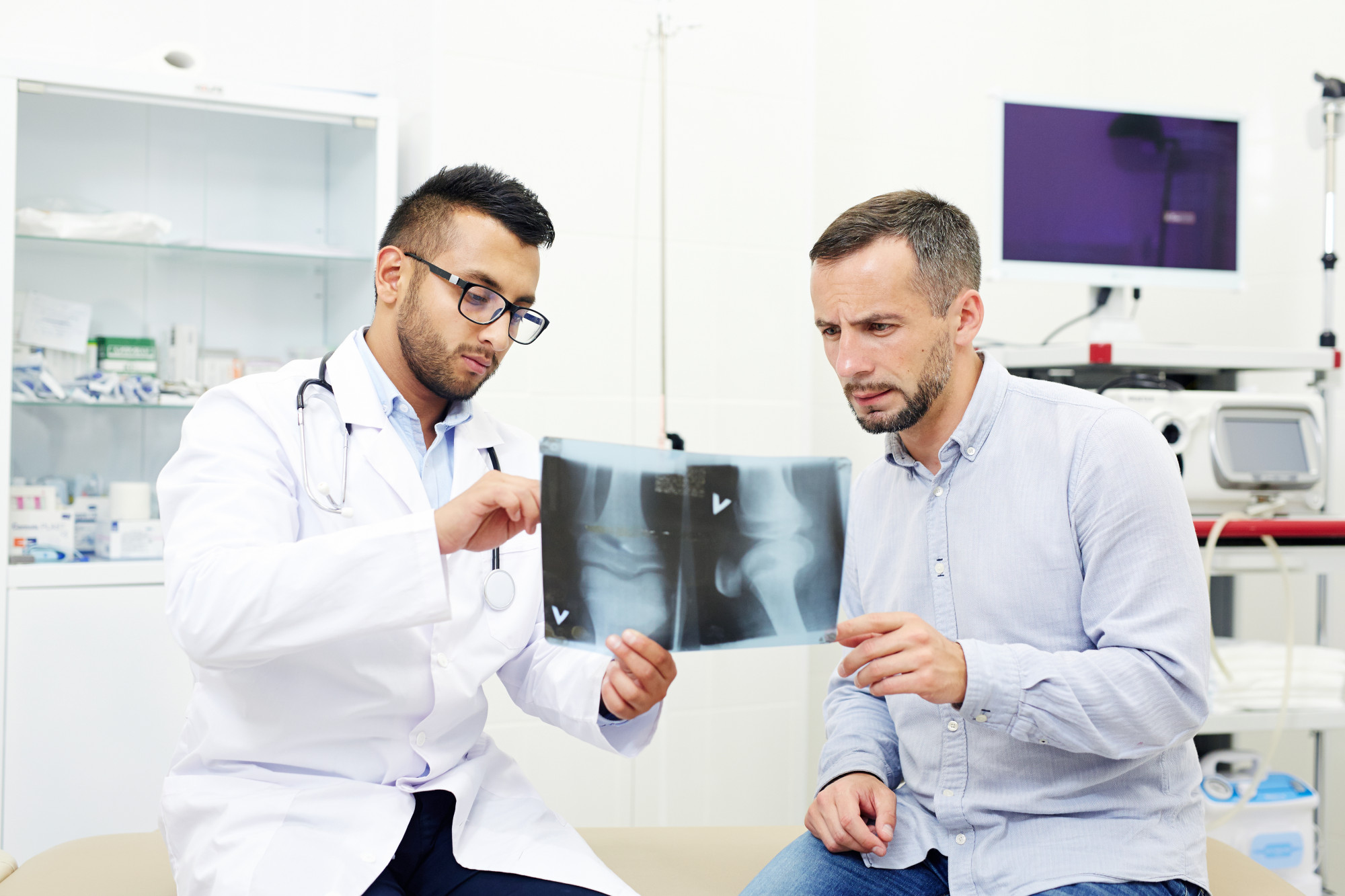A man is sitting with a doctor who is showing and explaining an X-ray report, discussing bone health or diagnosis.