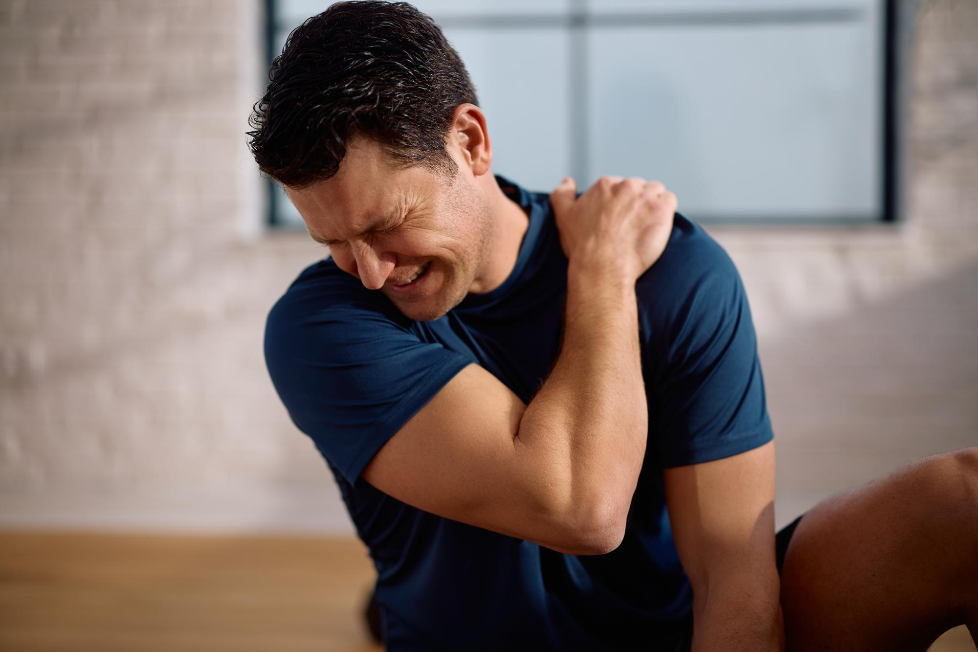 A man holding his shoulder with a tense expression, indicating muscle tightness or discomfort.
