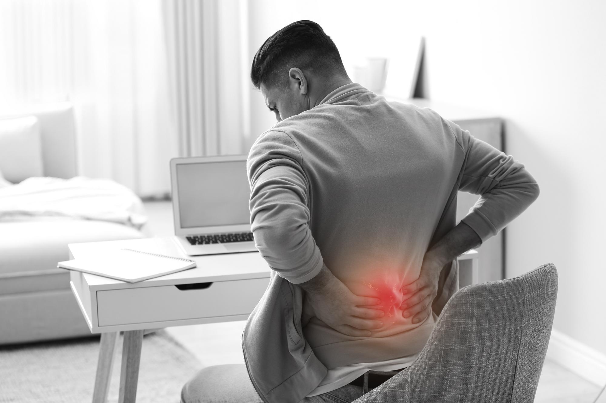 A man sitting at a desk with poor posture causing lower back strain.