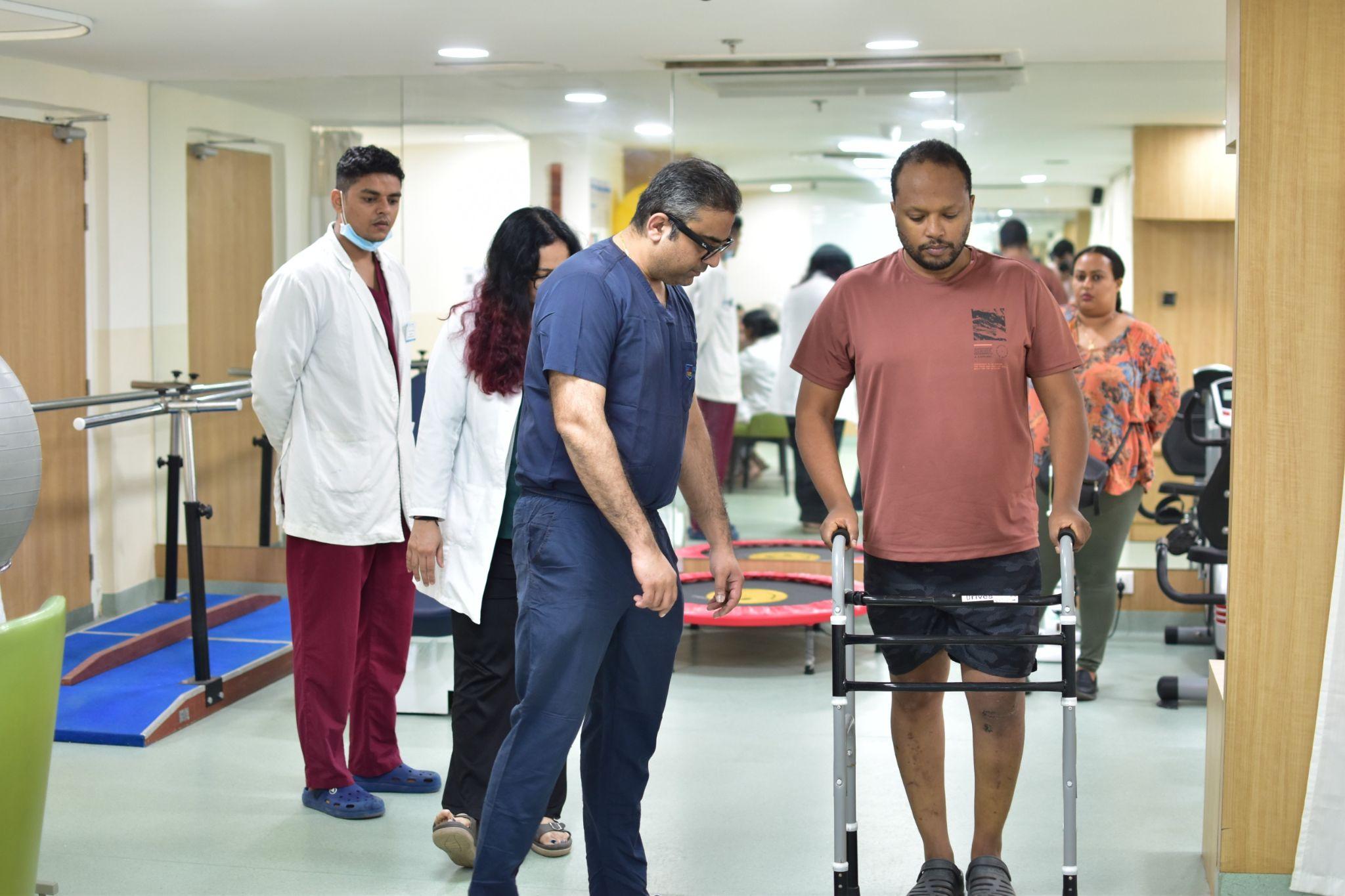 Dr. Ankur Singh guiding a patient with a walker, demonstrating dedicated orthopedic care and supportive rehabilitation after treatment.