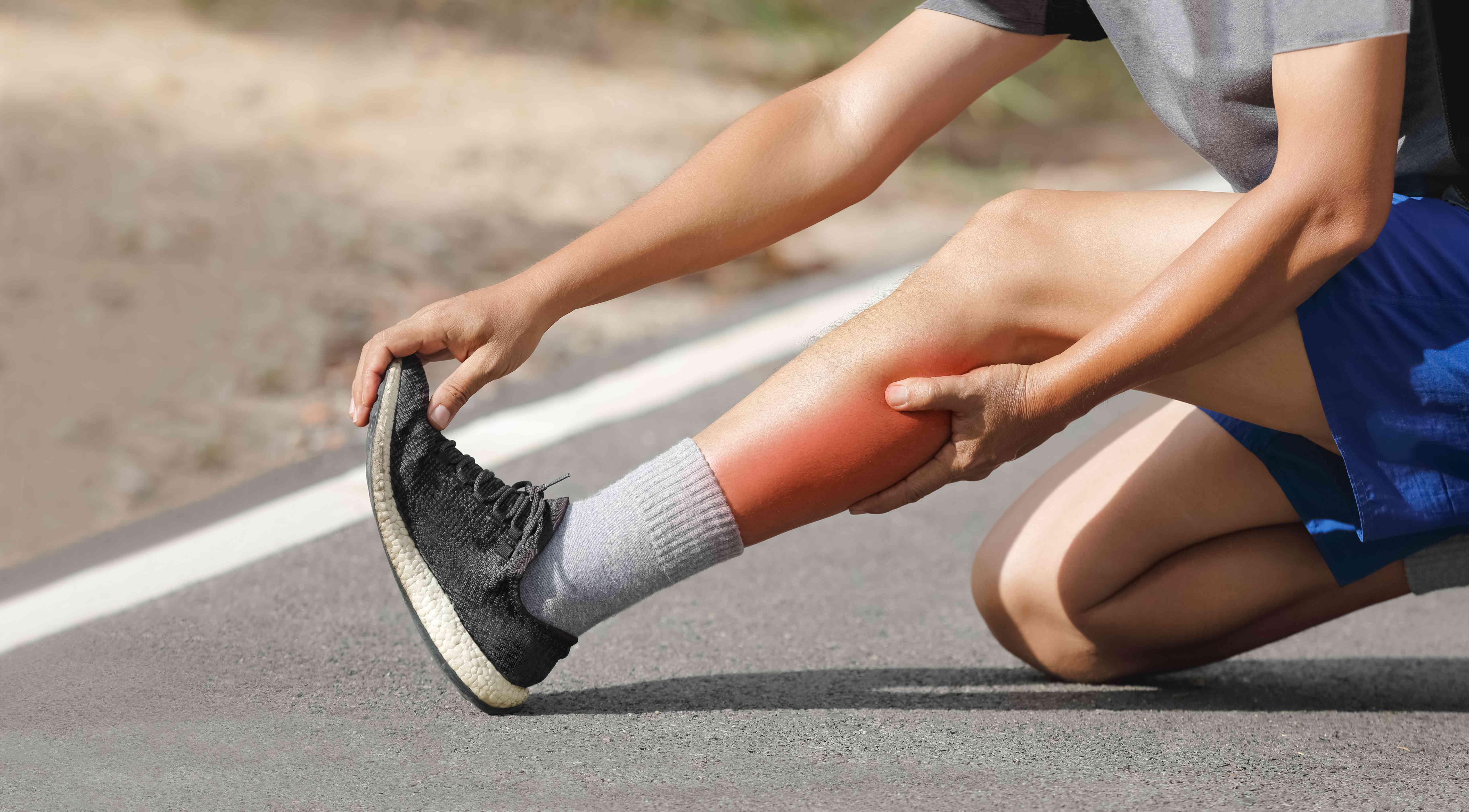 Athlete holding his sore lower leg on the roadside